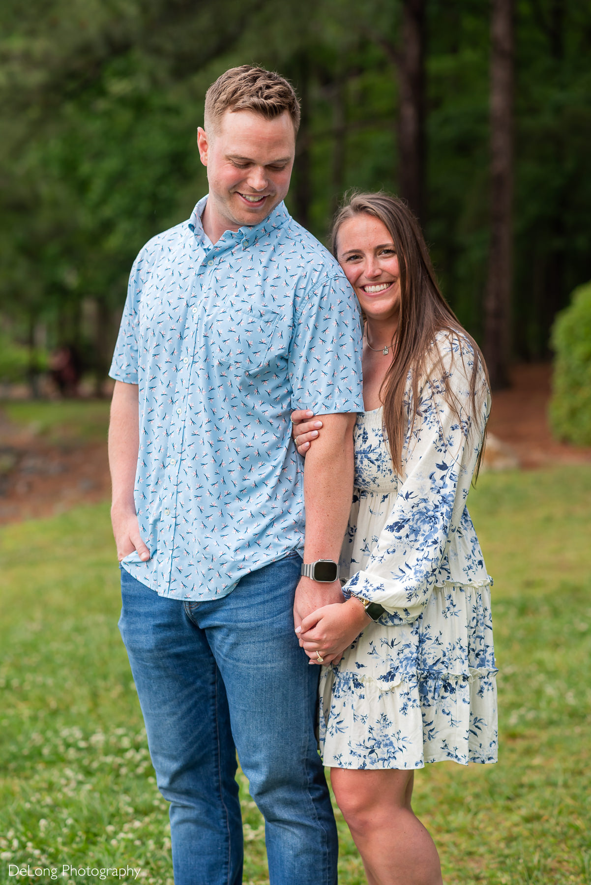 Man looking back his fiancée as she cuddles up on his arm from behind. She is smiling at the camera.