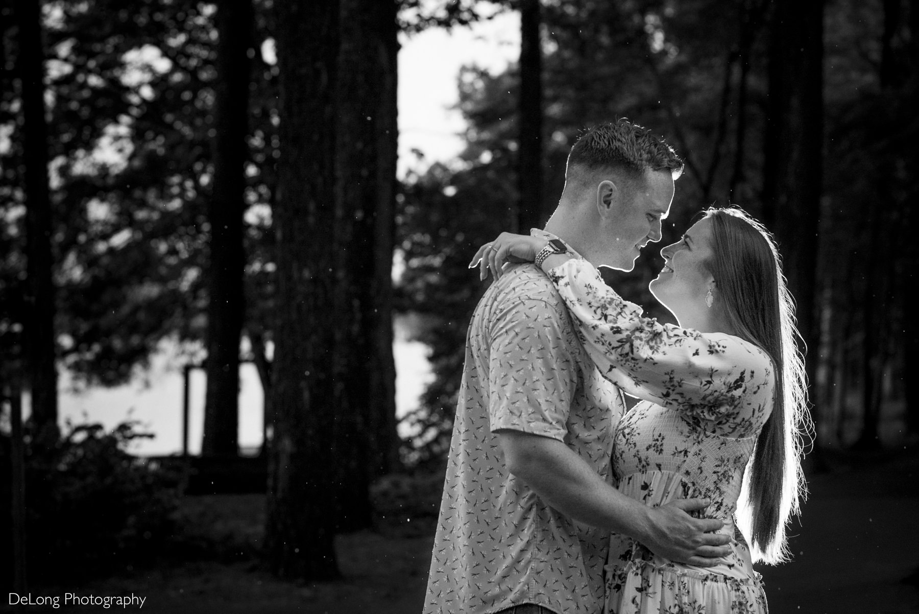 Black and white rim lit photograph of a newly engaged couple at Jetton Park. Their faces are close together, the woman's arms around her fiancé's neck. You can see droplets of rain around them.