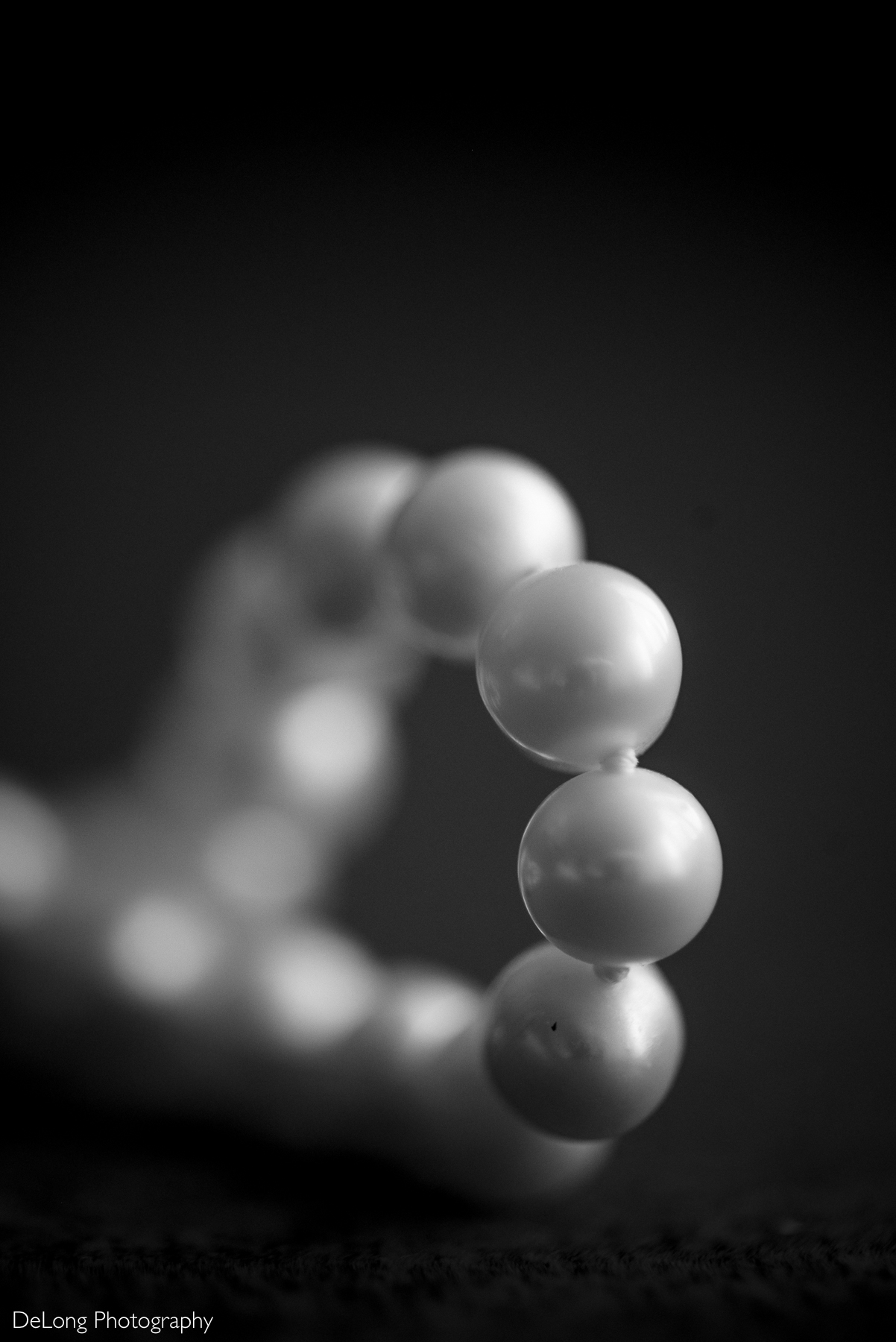 A delicate pearl bracelet elegantly draped and captured in black and white, showcasing its timeless beauty and soft luster. Photographed by DeLong Photography at the Kimpton Tryon Park Hotel.