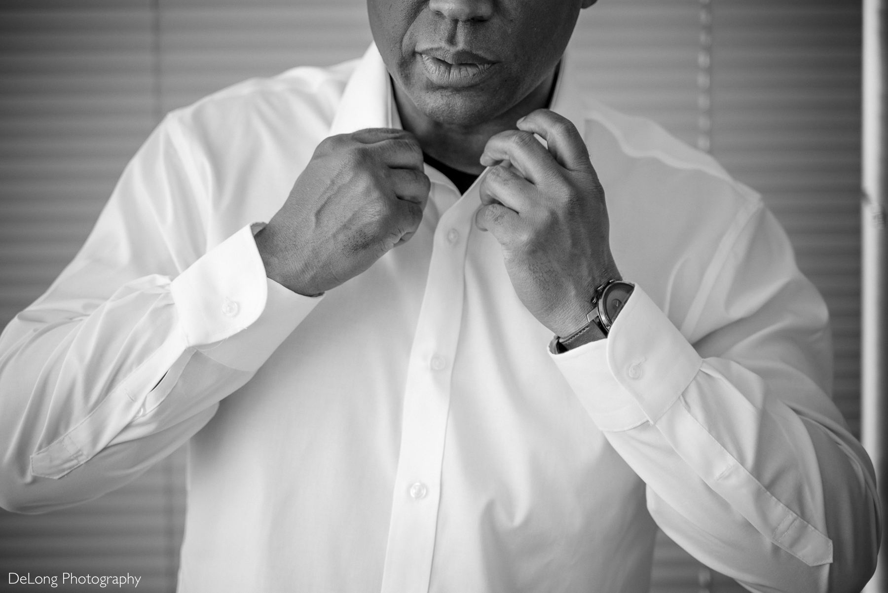 Black and white photograph of a groom adjusting his collar while getting ready at a condo in Uptown Charlotte. Captured by DeLong Photography.