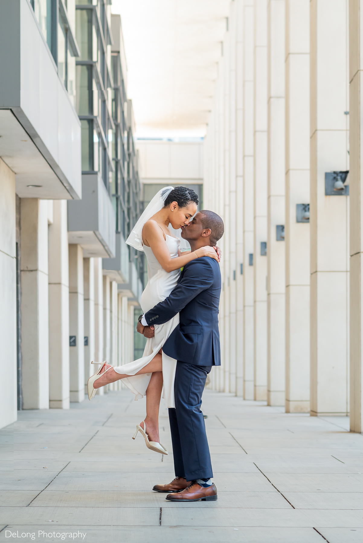 Groom lifts bride for a kiss in a sleek, architectural corridor in Uptown Charlotte. Captured by DeLong Photography, Charlotte elopement photographers specializing in stylish, city-chic wedding portraits for modern couples.