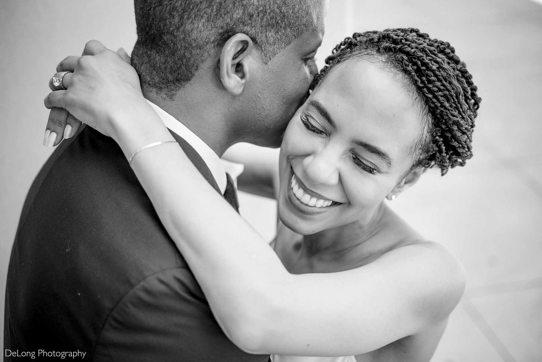 Black and white portrait of a bride smiling as she embraces her groom during their Uptown Charlotte elopement. Photographed by DeLong Photography, a Charlotte-based luxury wedding photographer specializing in intimate, elegant, and timeless wedding imagery for modern couples planning a North Carolina wedding.