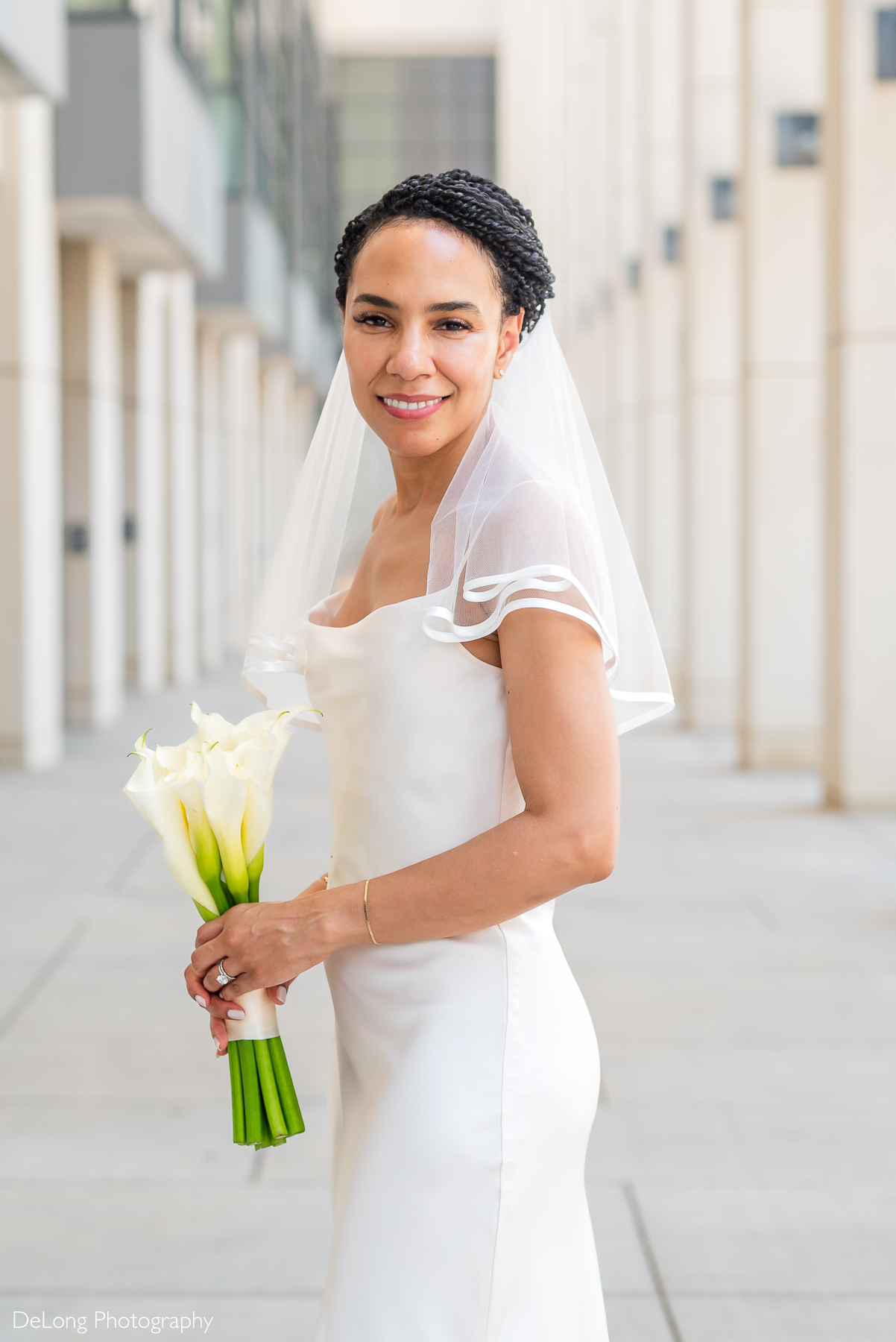 Elegant bride in a modern satin wedding dress holding calla lilies, captured in natural light at a luxury elopement in Uptown Charlotte by DeLong Photography, a husband-and-wife wedding photography team based in Charlotte, NC.