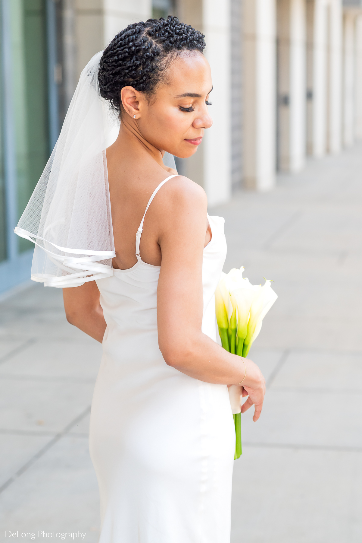 Modern bride holding calla lilies with a soft, romantic expression, photographed in natural light in Uptown Charlotte by DeLong Photography—Charlotte’s luxury husband-and-wife wedding photography team specializing in timeless, editorial-style portraits.