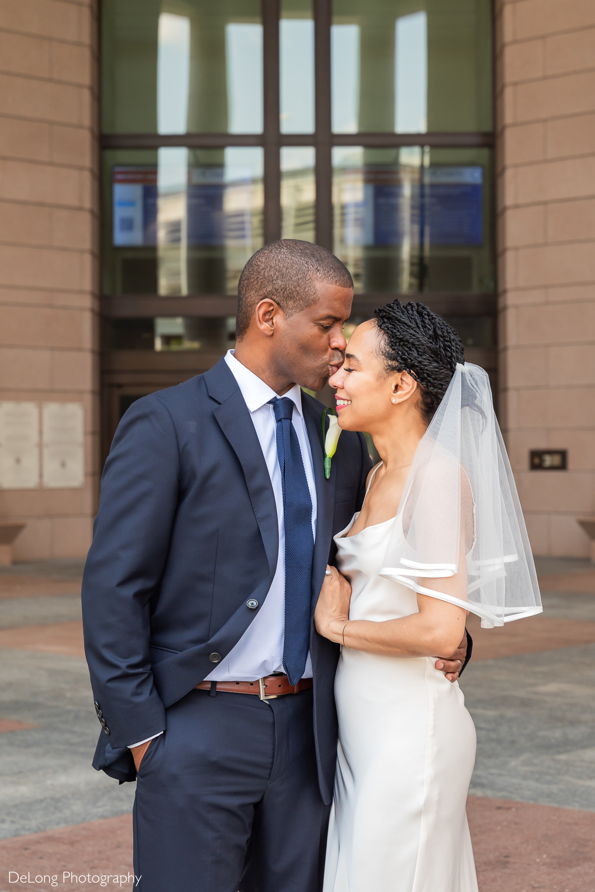 Romantic courthouse elopement at Mecklenburg County Courthouse captured by luxury Charlotte elopement photographer. Groom kisses bride's forehead in an elegant, modern wedding moment perfect for stylish, intimate celebrations in Uptown Charlotte.