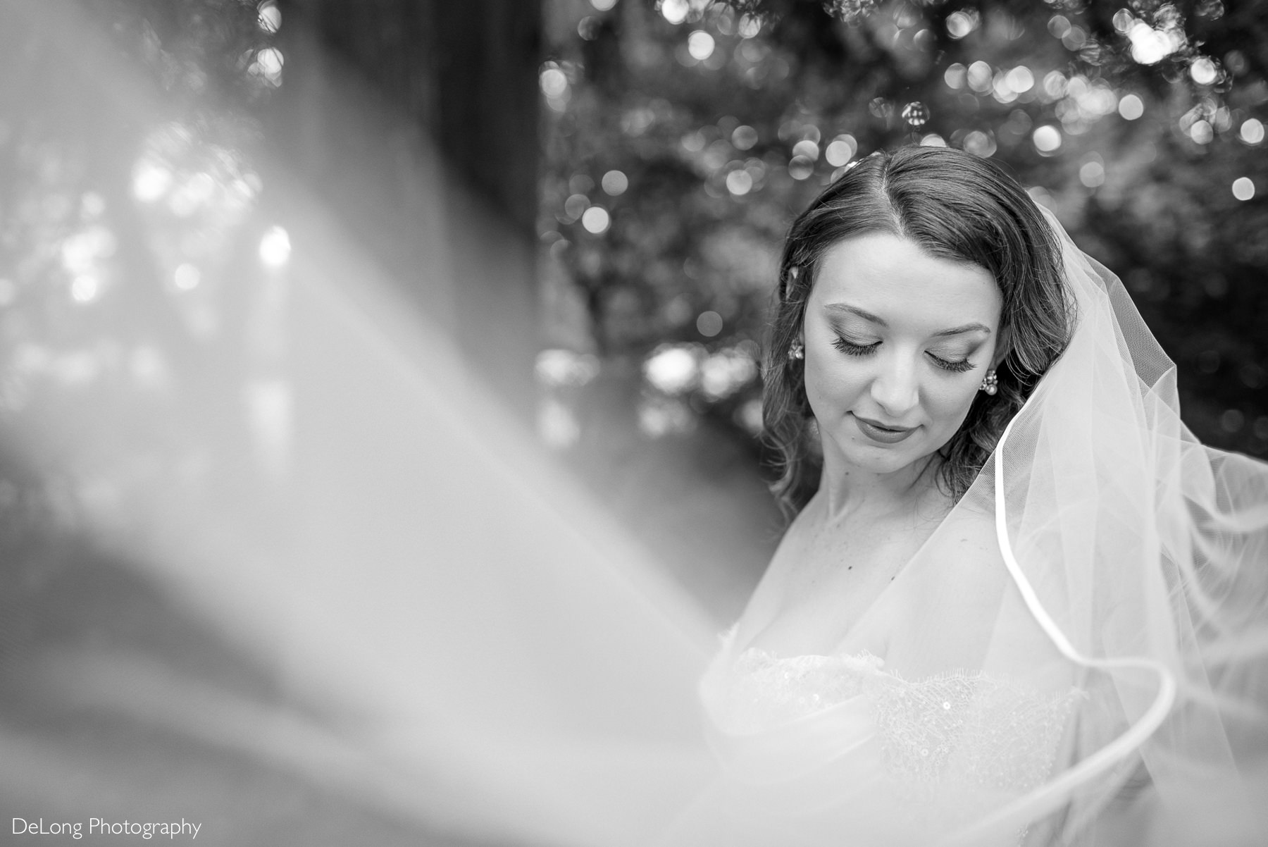 Black and white bridal portrait captured at The White Home in Rock Hill, SC, featuring a bride softly smiling with her eyes closed as her veil flows gracefully across the frame, creating an ethereal, romantic atmosphere. Photographed by DeLong Photography.