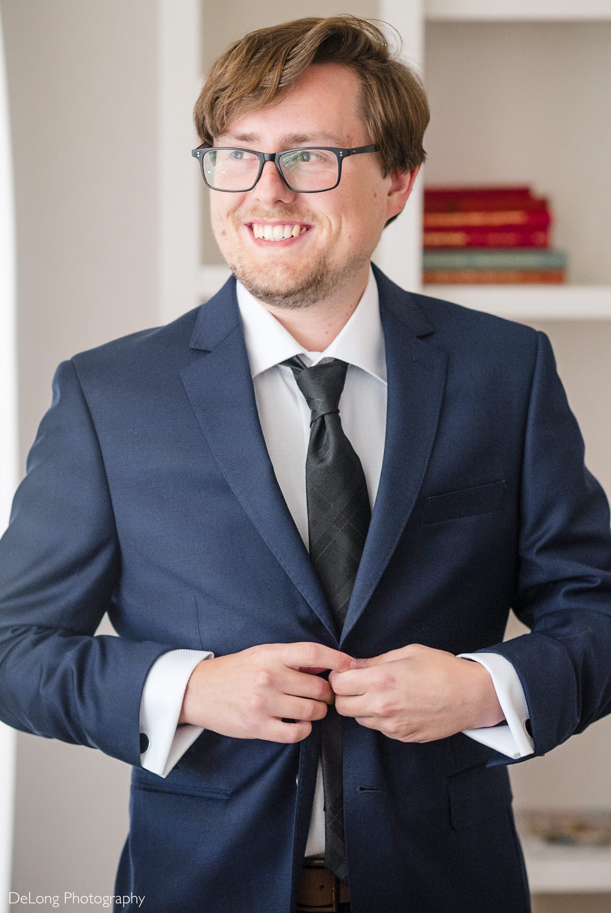 Groom smiling while buttoning his navy suit jacket before his fall courthouse elopement at the Wake County Courthouse in Raleigh, North Carolina, photographed by DeLong Photography.