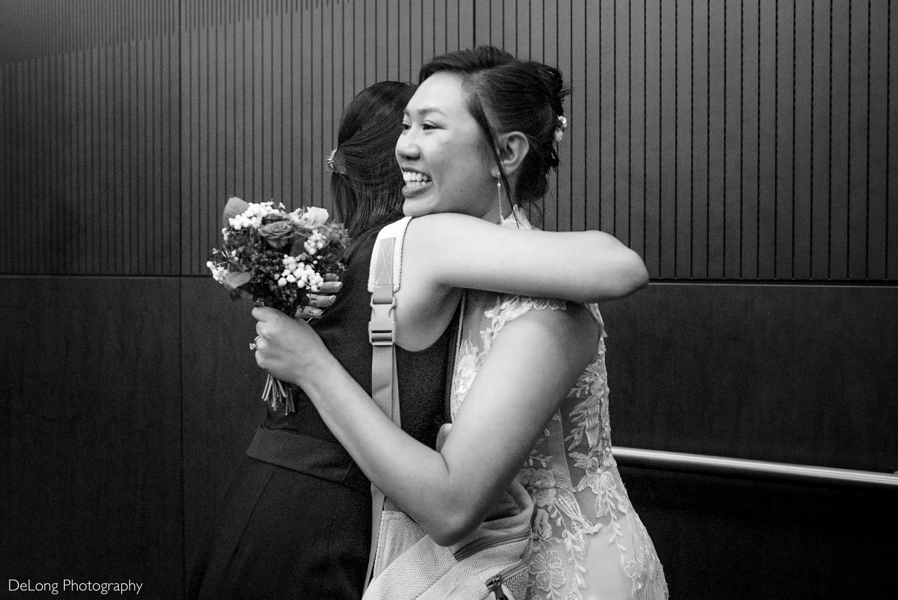 Bride beams with joy as she hugs a guest while holding her bouquet during a Raleigh elopement at the Wake County Courthouse — candid moment captured by DeLong Photography.