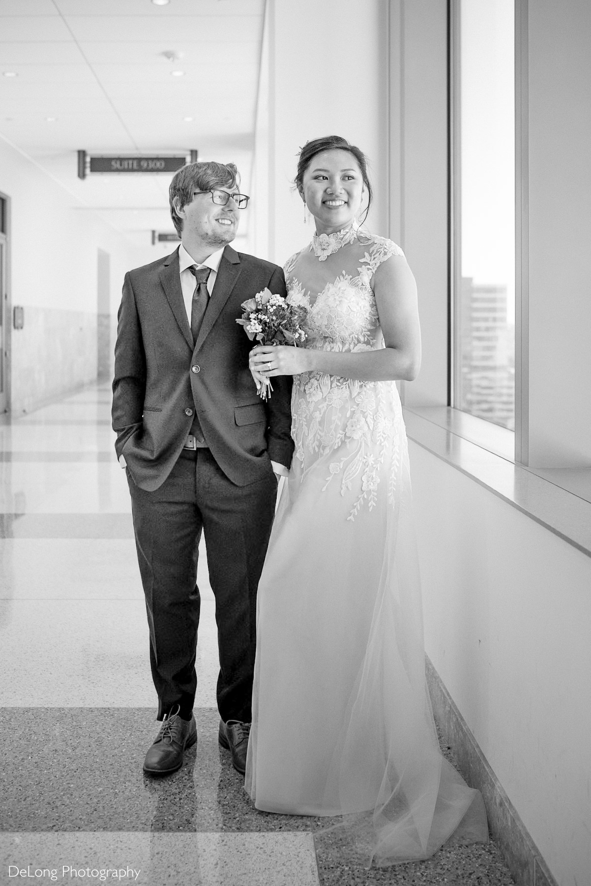 Bride and groom share a joyful moment after their Wake County Courthouse elopement in Raleigh, NC. The bride wears a lace wedding dress and holds a small bouquet, while the groom smiles in a suit and tie. Captured by DeLong Photography.