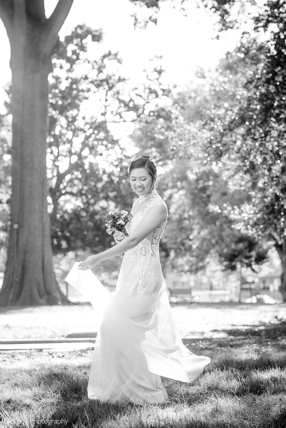 Bride twirling in her wedding jumpsuit at a sunny park near the Wake County Courthouse during a Raleigh elopement. Captured by DeLong Photography in a romantic black and white portrait.