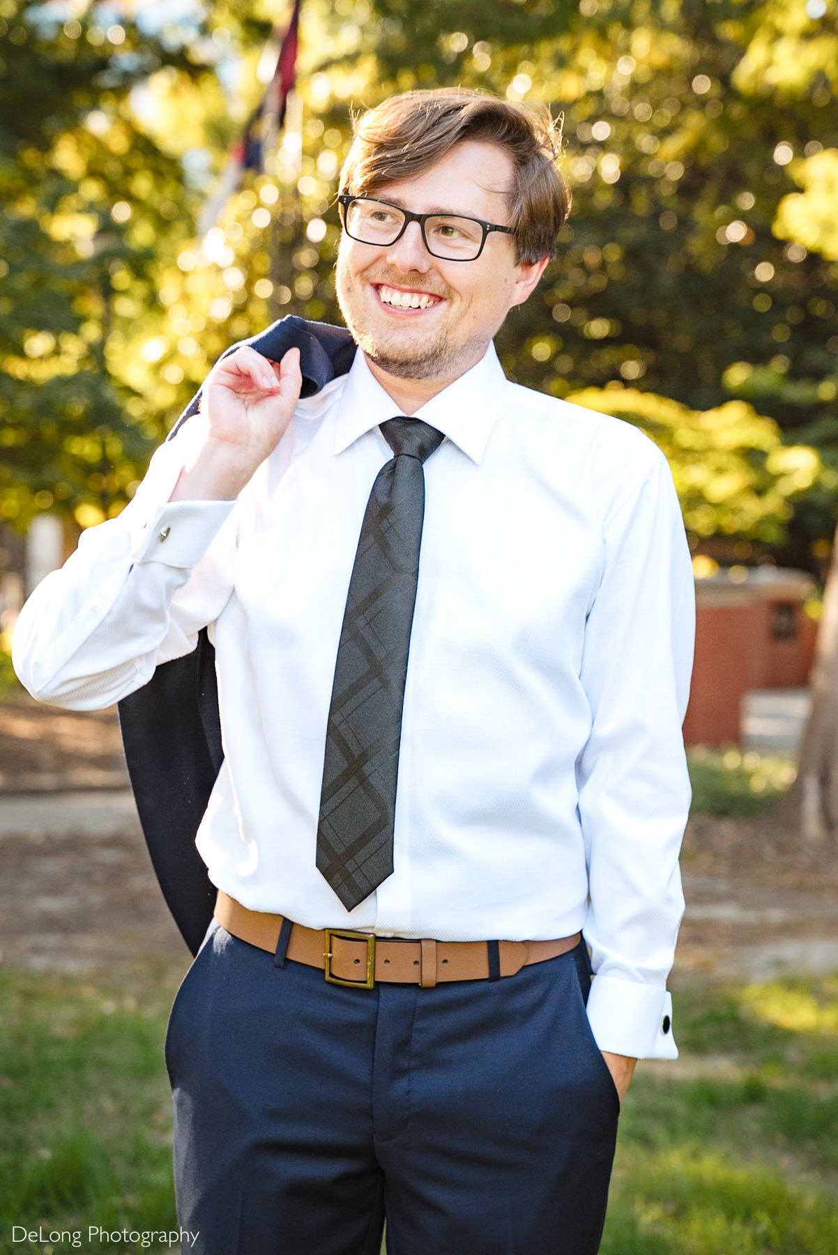 Groom smiling and holding his jacket over his shoulder during a sunny downtown Raleigh courthouse elopement. Captured outside the Wake County Courthouse by DeLong Photography.
