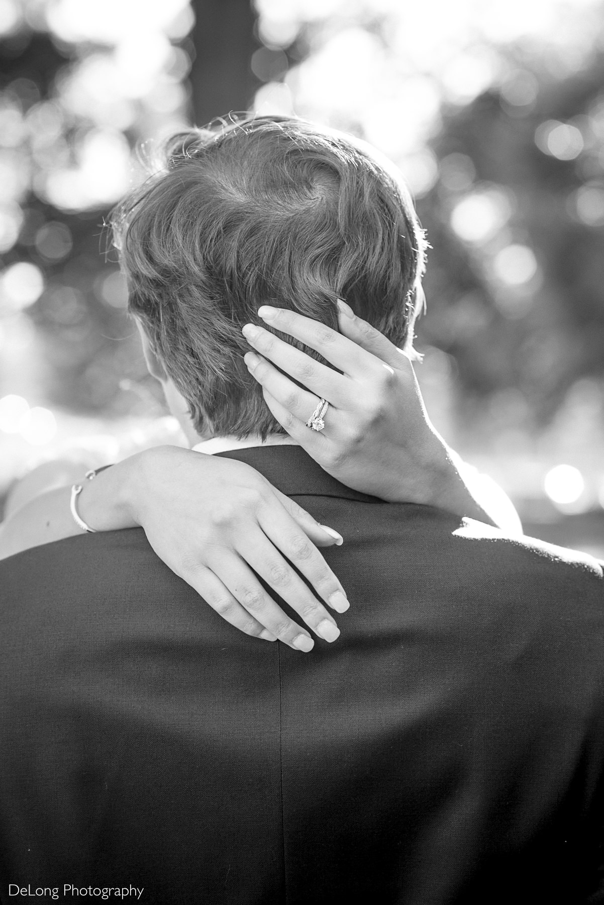 Bride embraces groom from behind, showcasing her engagement ring in a romantic black and white portrait during their Raleigh courthouse elopement at Nash Square. Captured by DeLong Photography.
