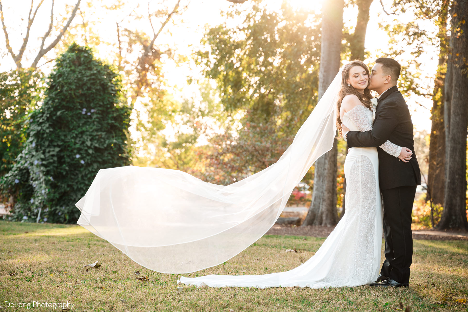 Bride and groom at The White Home in Rock Hill during golden hour, with the bride’s long veil flowing in the breeze. Captured by Charlotte wedding photographer DeLong Photography.