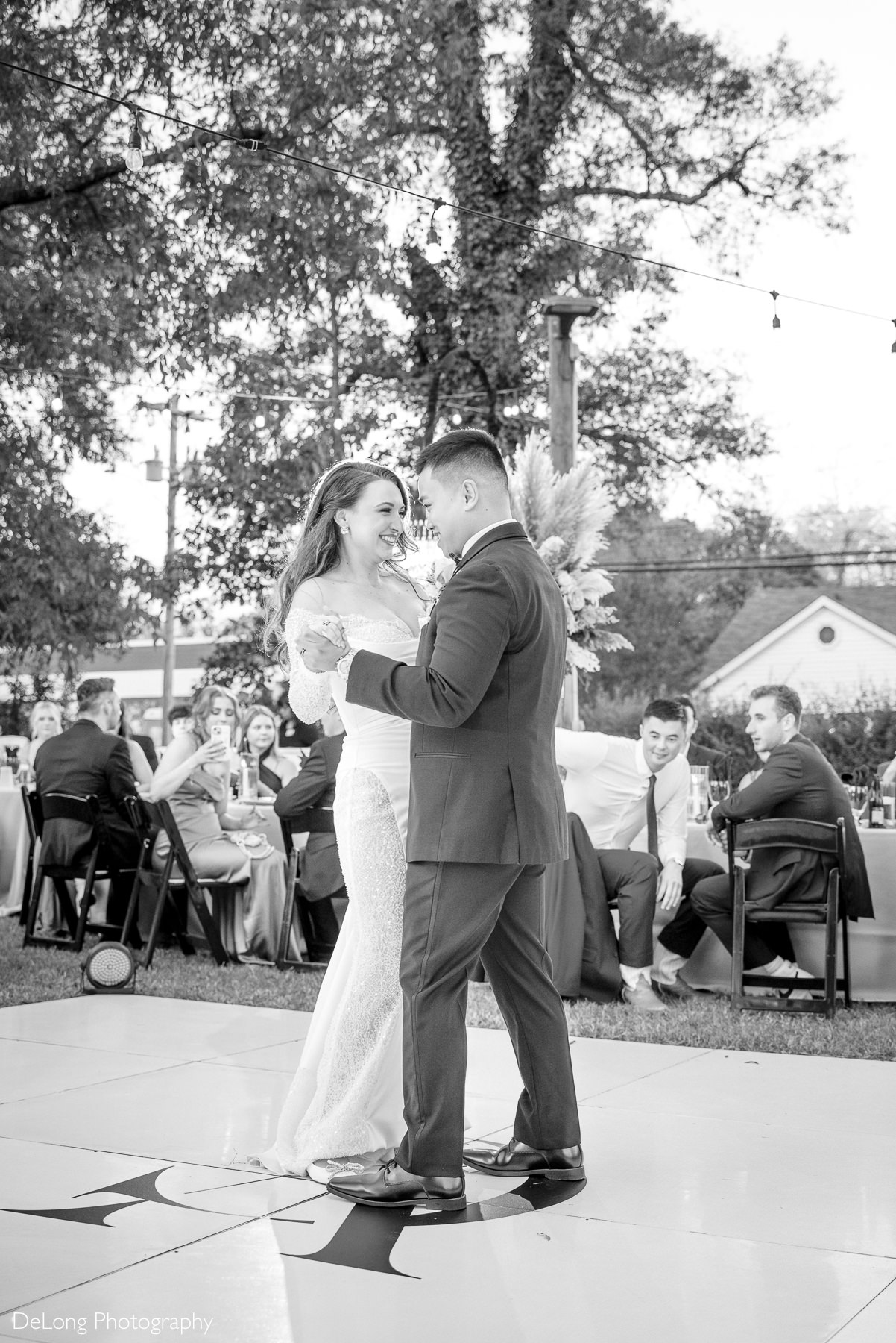 Bride and groom sharing their first dance outdoors at The White Home in Rock Hill, smiling joyfully on a custom monogrammed dance floor surrounded by guests.