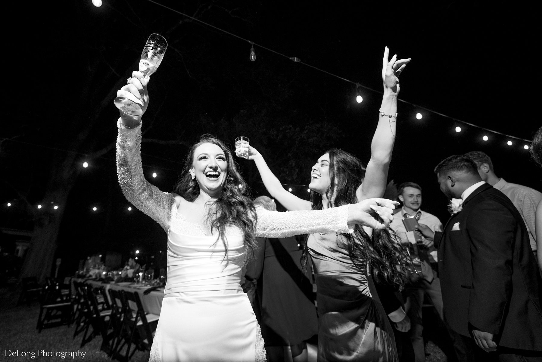 Bride celebrates on the dance floor with bridesmaid and guests during outdoor wedding reception at The White Home in Rock Hill.