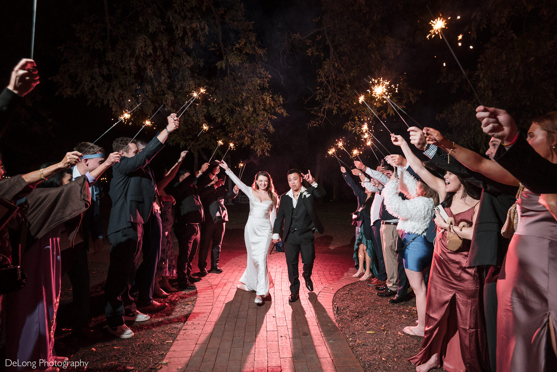 Bride and groom walk hand in hand through a sparkler exit surrounded by cheering guests at The White Home in Rock Hill.