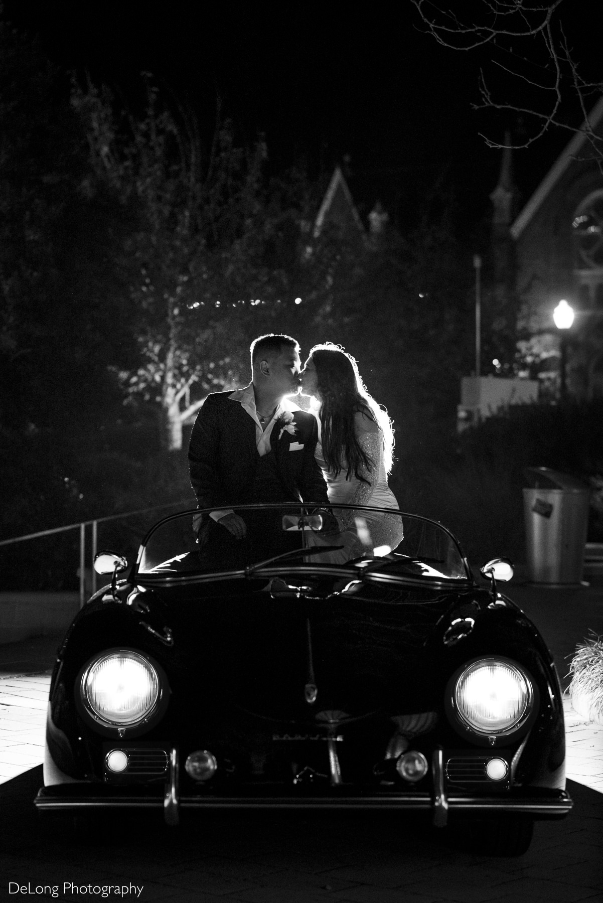 Bride and groom kiss while sitting on vintage Porsche getaway car at night during Rock Hill wedding.