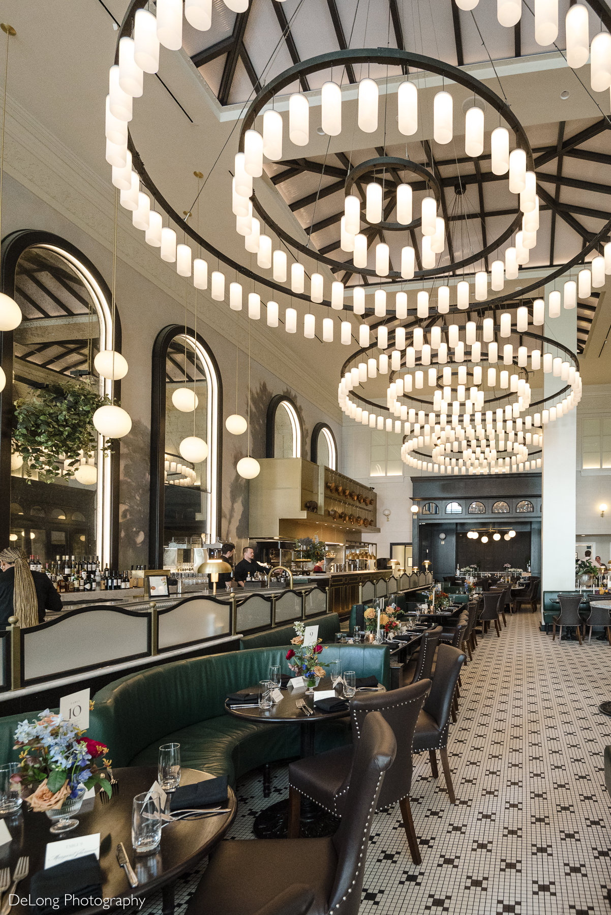 Interior of La Belle Helene in Charlotte, NC, featuring grand circular chandeliers, elegant brasserie décor, and beautifully set tables—an ideal restaurant venue for intimate wedding receptions and upscale celebration dinners.