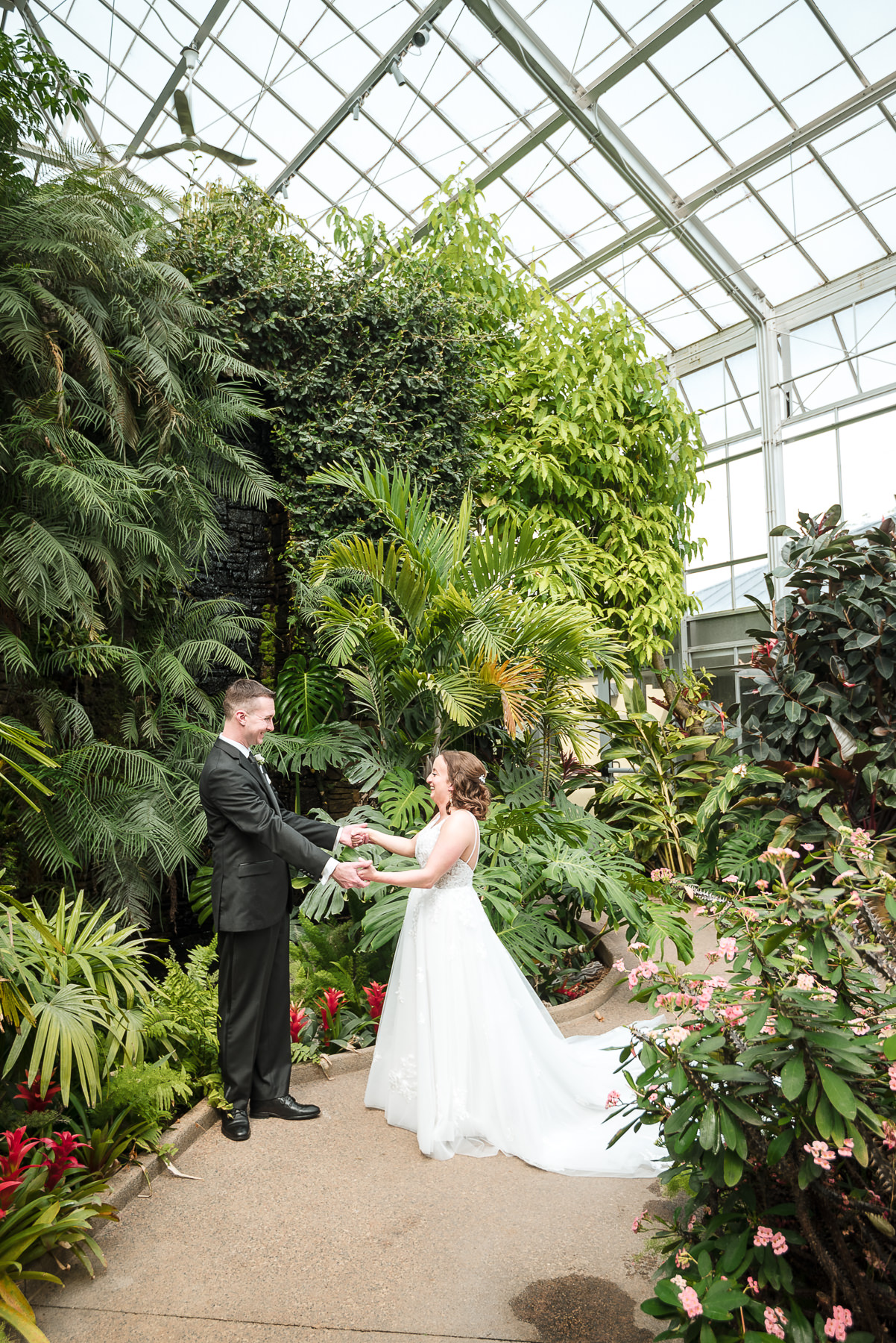 Bride and groom share a first look inside the greenhouse at Daniel Stowe Botanical Garden in Belmont, NC during a spring wedding, surrounded by lush tropical greenery and natural light.