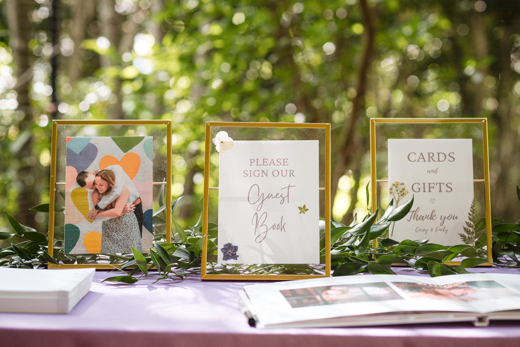 Wedding guest book table display with gold frames, engagement photo, and “Please Sign Our Guest Book” and “Cards and Gifts” signs at a spring wedding at Daniel Stowe Botanical Garden in Belmont, NC. 
