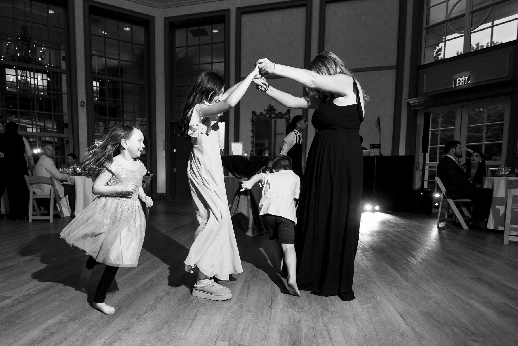 Black and white photo of children and guests dancing at a spring wedding reception at Daniel Stowe Botanical Gardens in Belmont, NC, photographed by DeLong Photography in the glass conservatory.