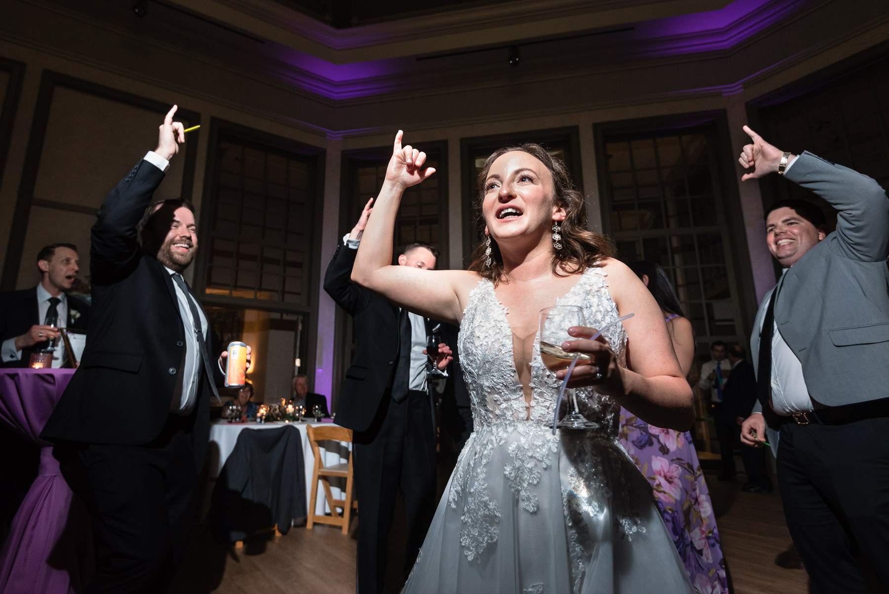 Bride dancing with guests at a spring wedding reception at Daniel Stowe Botanical Gardens in Belmont, NC, with purple uplighting inside the glass conservatory.