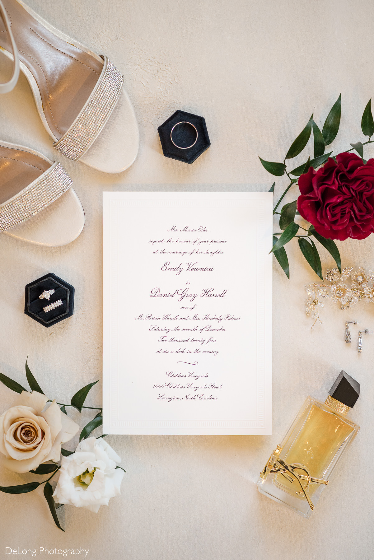Flat lay of wedding invitation, rings, bridal shoes, florals, and perfume from a Christmas-themed wedding at Childress Vineyards in Lexington, North Carolina, photographed by DeLong Photography.