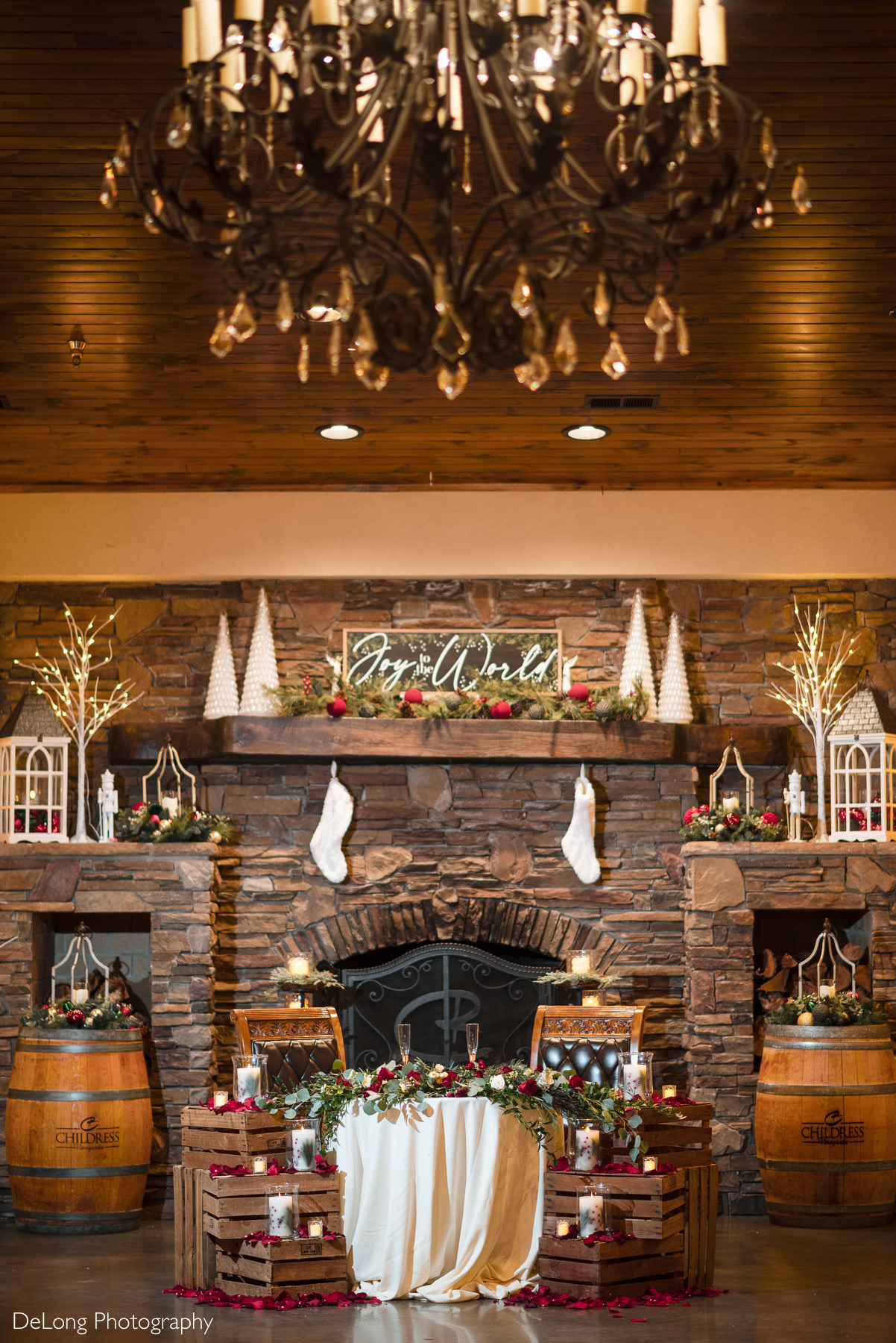 Christmas-themed sweetheart table at a Childress Vineyards wedding in Lexington, North Carolina, styled in front of a stone fireplace with festive greenery, candles, and wine barrels, photographed by DeLong Photography.