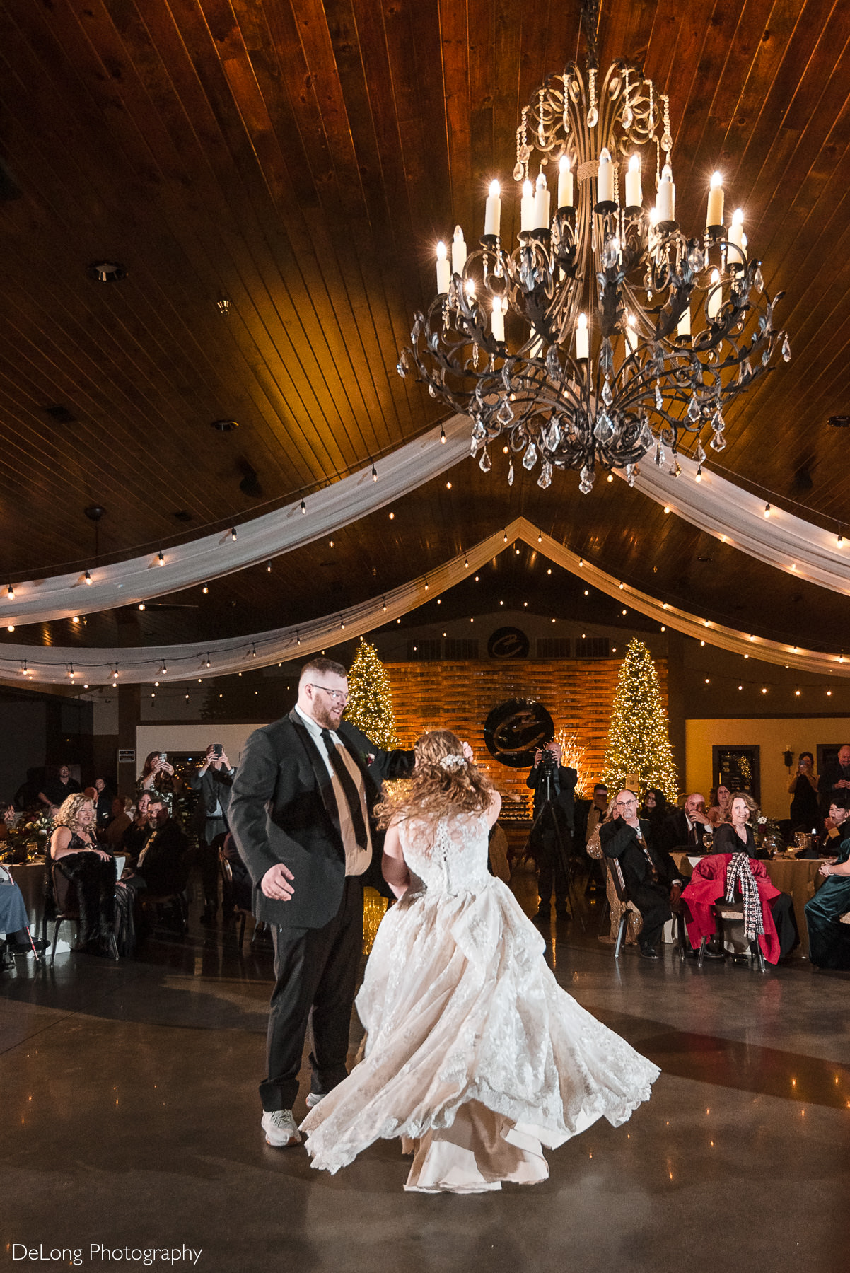 Bride twirls during the couple’s first dance at Childress Vineyards in Lexington, North Carolina, beneath a crystal chandelier and warm string lights during their winter wedding reception.