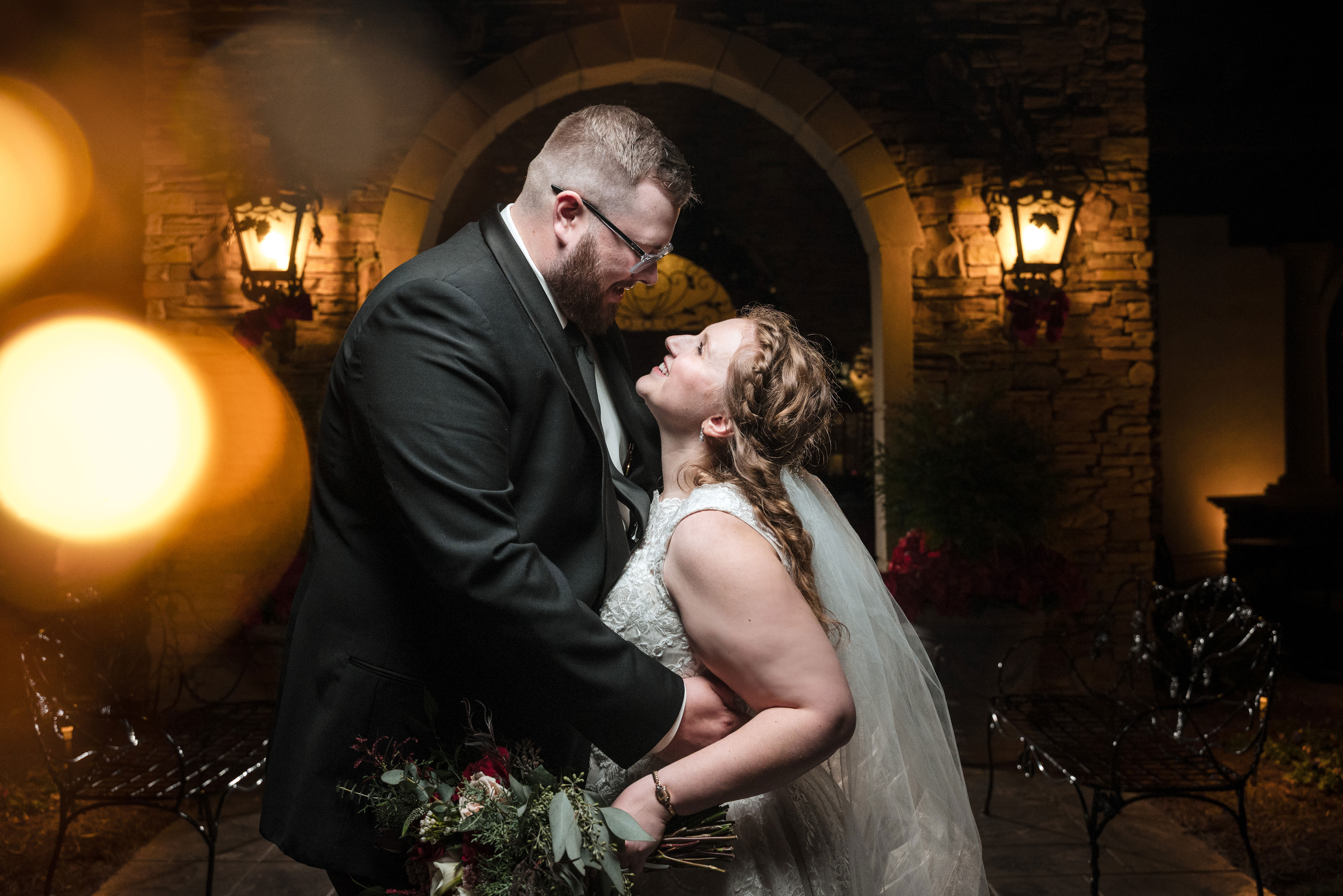 Romantic nighttime wedding portrait of a bride and groom embracing beneath a stone archway at Childress Vineyards in Lexington, North Carolina, softly lit with warm lights and captured by DeLong Photography.