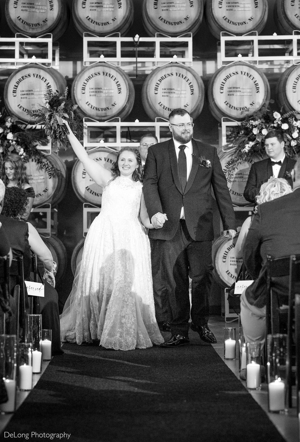 Bride and groom walk down the aisle hand in hand during their Childress Vineyards wedding ceremony in Lexington, North Carolina, celebrating their newlywed moment in front of wine barrels and guests.