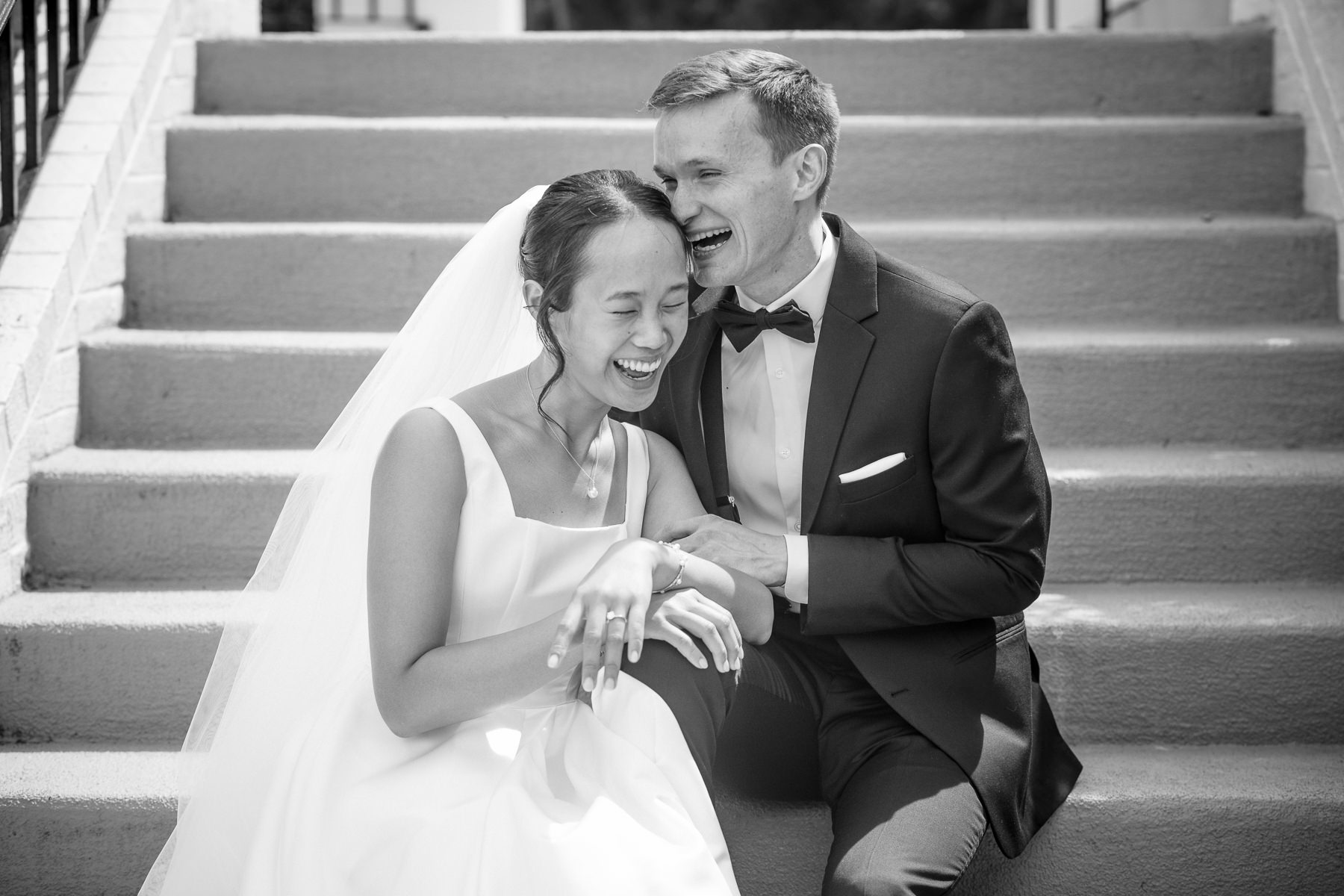 Bride and groom laughing together on the steps at Providence Country Club in Charlotte, NC during their wedding day portrait session captured by DeLong Photography. This timeless black-and-white wedding photo highlights DeLong Photography as a Charlotte wedding photographer for couples seeking candid and elegant wedding photography in the Charlotte area.