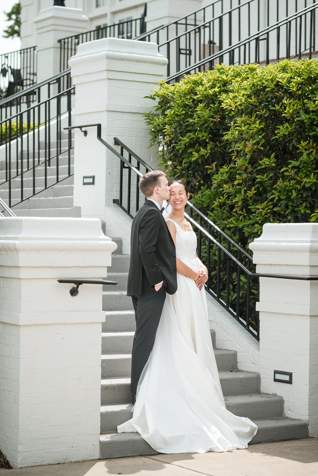 Bride and groom share a joyful moment on the staircase at Providence Country Club during their elegant Charlotte, NC wedding, captured by DeLong Photography. Romantic wedding portraits like this showcase the timeless style and candid storytelling couples look for in a Charlotte wedding photographer.
