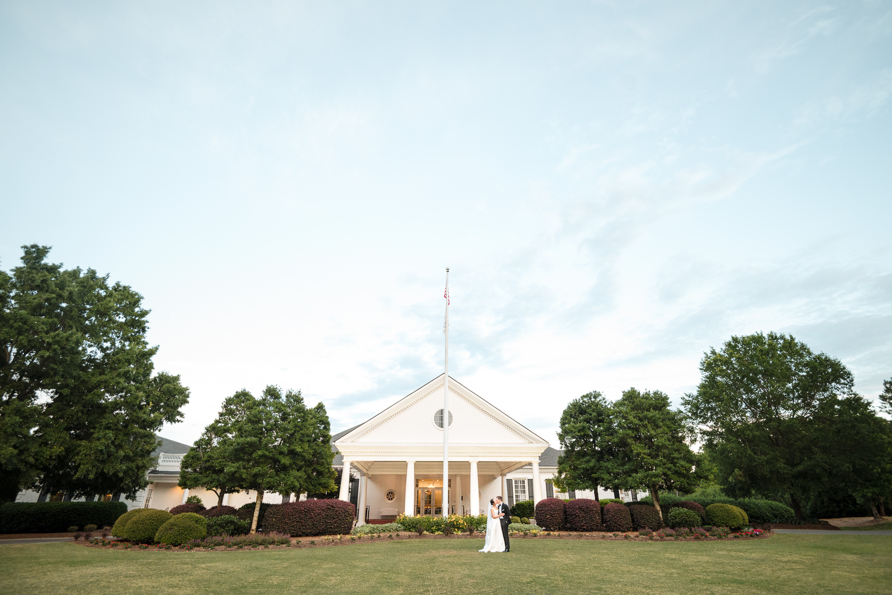 Bride and groom share an intimate moment on the lawn in front of the clubhouse during a Providence Country Club wedding in Charlotte, North Carolina. Elegant outdoor wedding portrait photography by DeLong Photography showcases the classic architecture and serene country club setting.