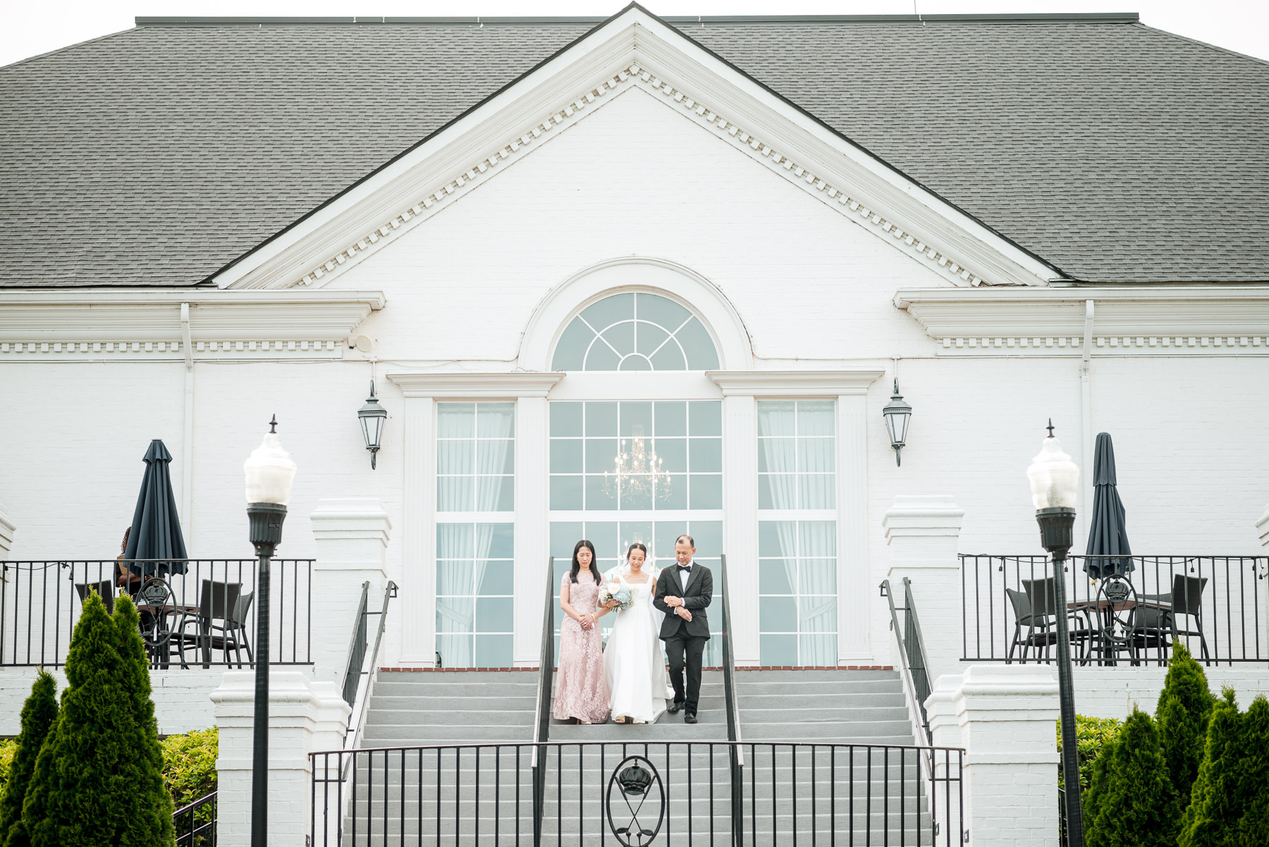 Bride walking down the grand staircase outside Providence Country Club before her outdoor wedding ceremony, photographed by DeLong Photography, a Charlotte wedding photographer specializing in elegant country club weddings and timeless wedding photography in Charlotte, NC.