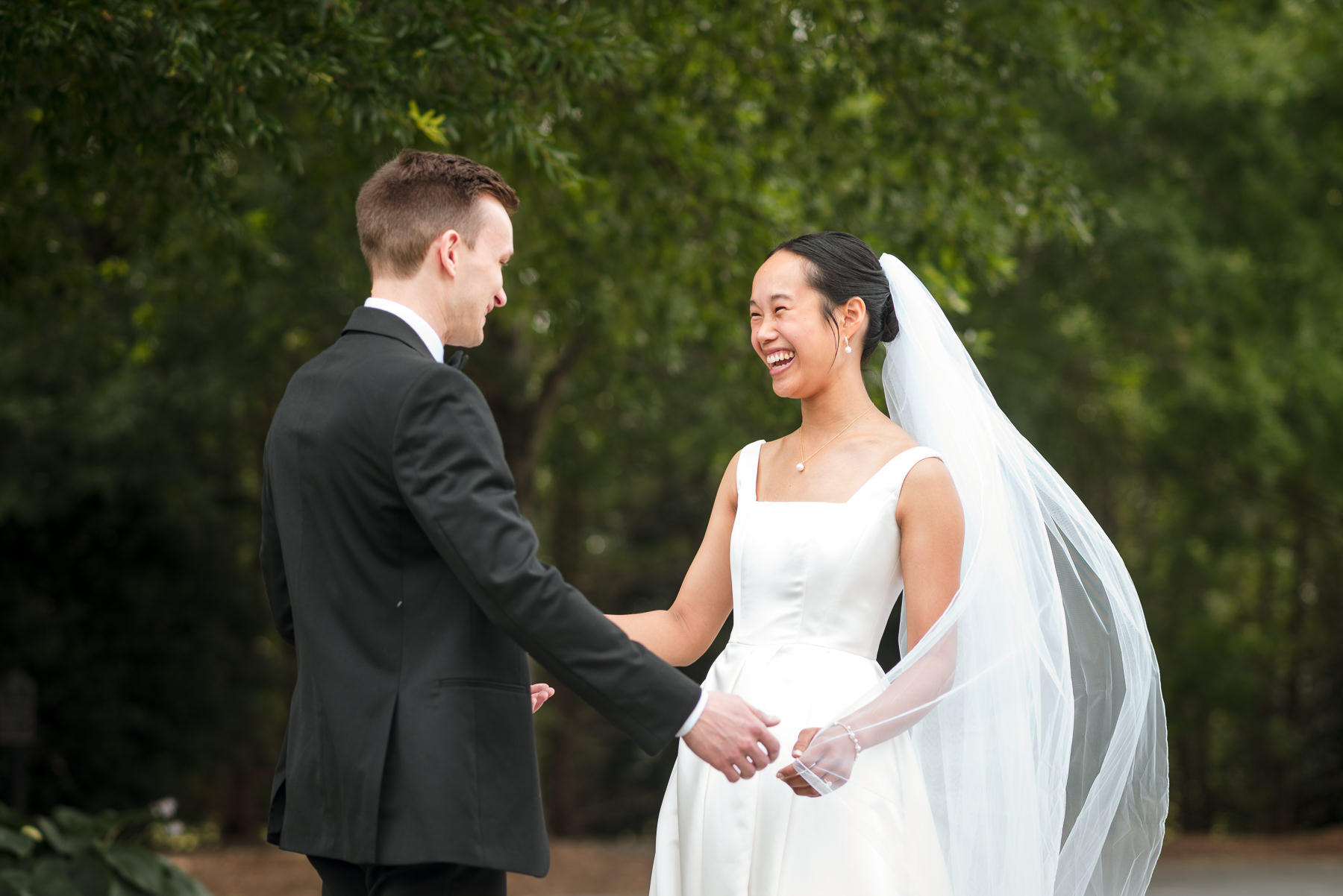 Bride and groom smiling during their first look at Providence Country Club in Charlotte, NC, captured by DeLong Photography. The couple shares an emotional moment outdoors surrounded by lush greenery during their elegant country club wedding.