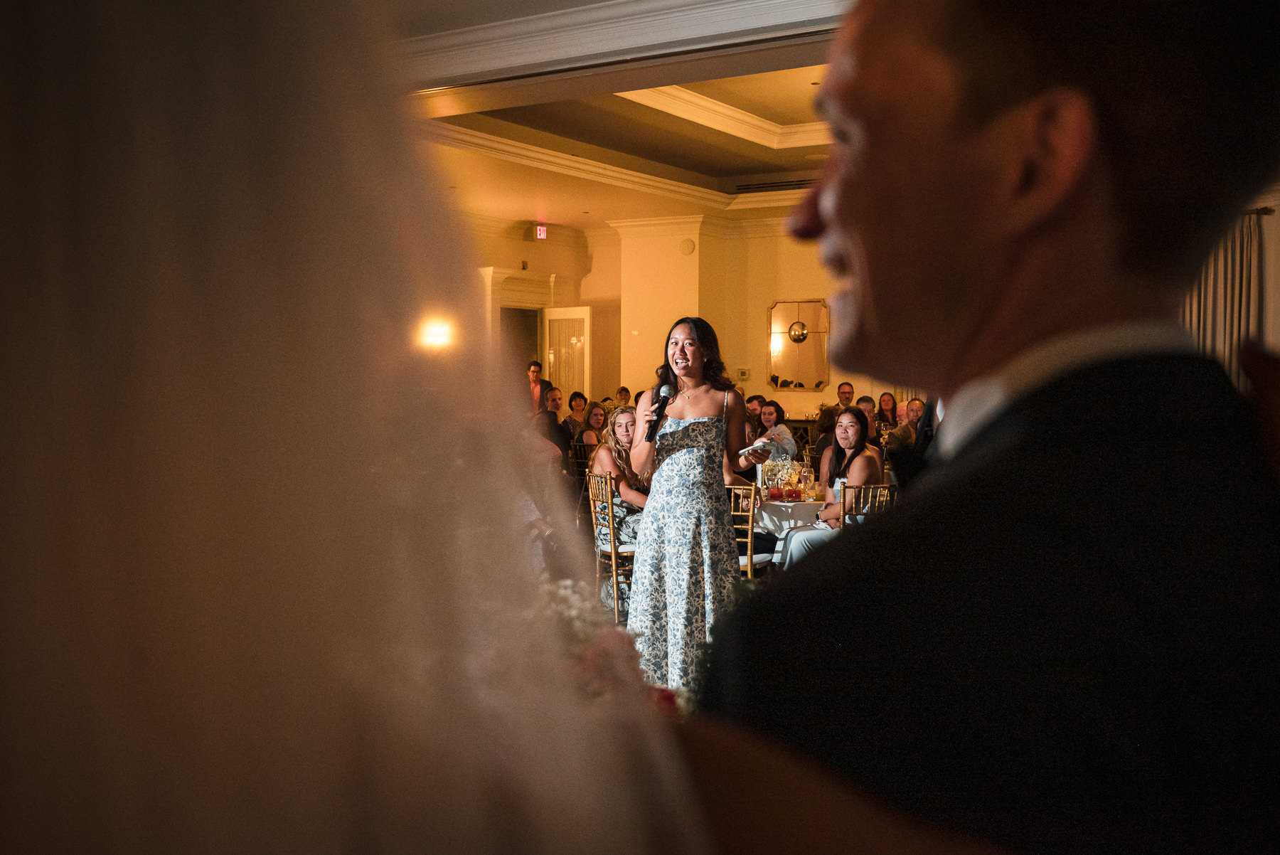 Wedding guest gives a heartfelt reception toast as the bride and groom listen during an elegant wedding celebration at Providence Country Club, photographed by DeLong Photography in Charlotte, NC. This candid wedding reception photography captures the emotional storytelling couples look for when searching for Charlotte wedding photographers.