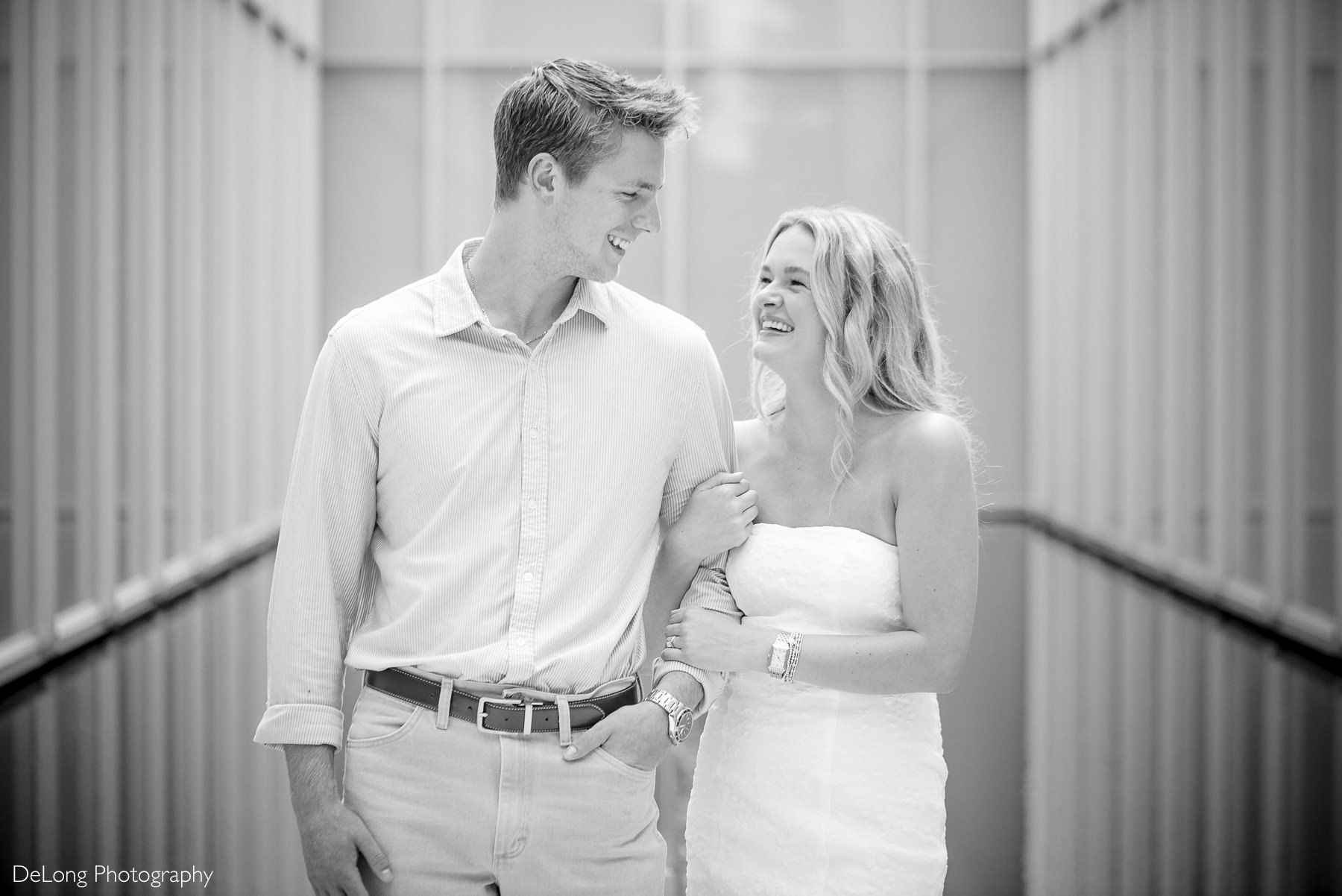 Raleigh engagement photos at the North Carolina Museum of Art featuring a joyful couple walking arm in arm through the museum’s modern architectural walkway during their engagement session. Captured by DeLong Photography, these natural and romantic Raleigh engagement photos showcase authentic connection and timeless engagement photography in the Raleigh area.