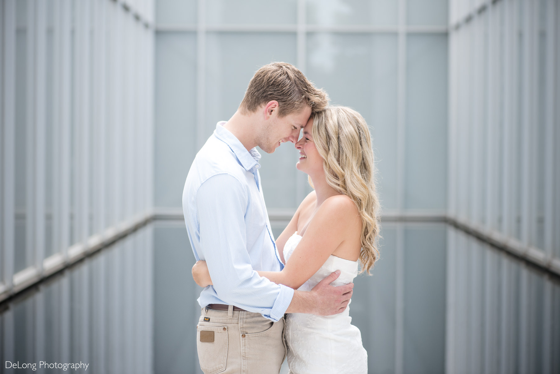 Engaged couple sharing a joyful embrace inside the modern architecture of the North Carolina Museum of Art during their Raleigh engagement session. Captured by DeLong Photography, a Raleigh engagement photographer specializing in timeless and authentic engagement photos in North Carolina.