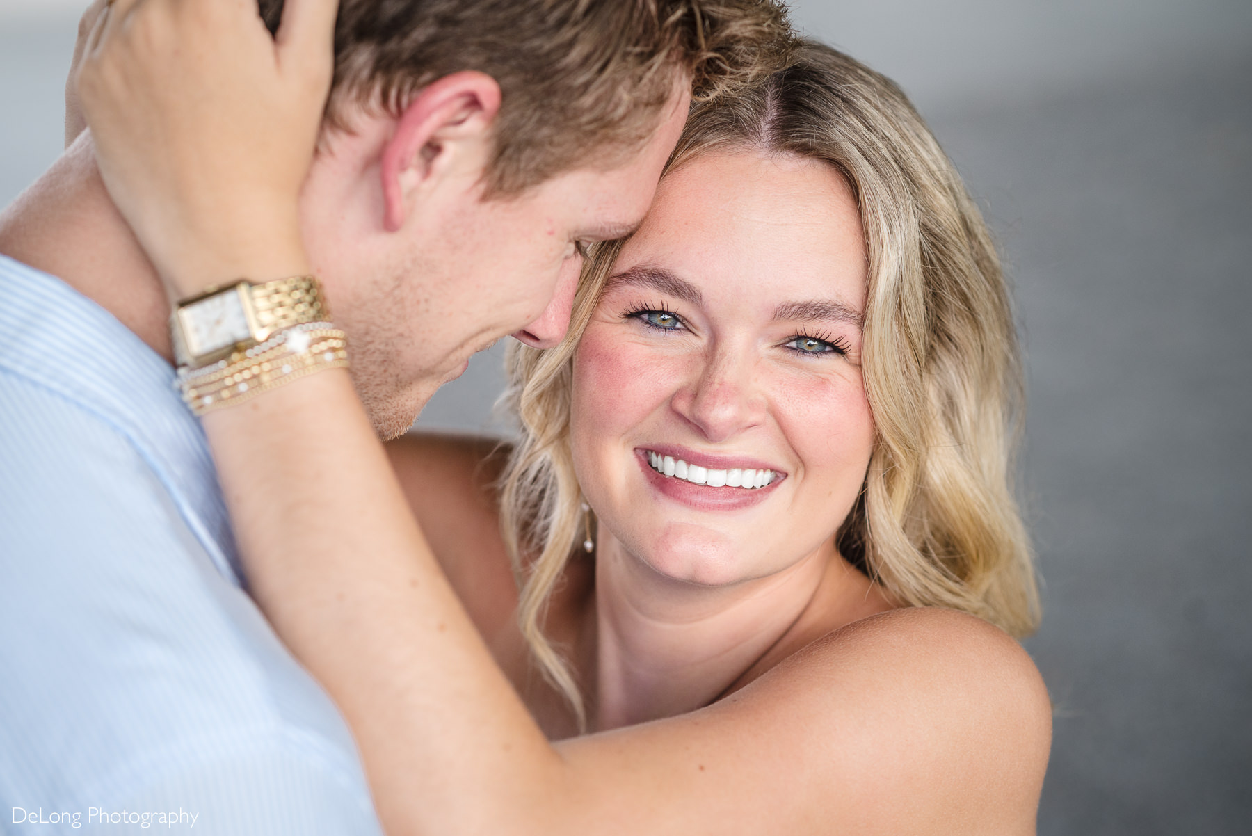 Close-up portrait of an engaged couple during a North Carolina Museum of Art engagement session in Raleigh, NC, with the bride-to-be smiling at the camera while embracing her fiancé. Captured by DeLong Photography during a timeless and romantic engagement session.