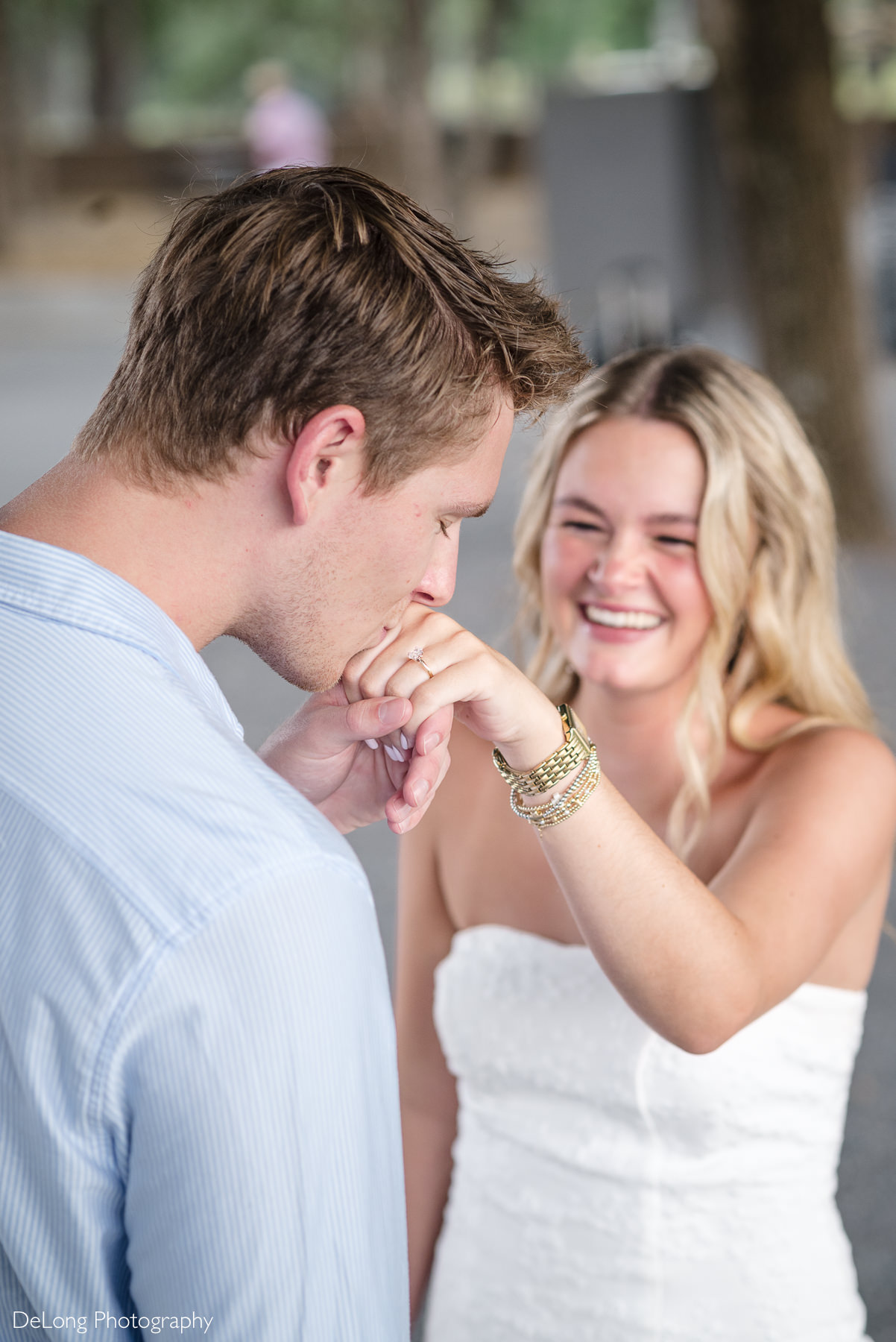 Close-up portrait of an engaged couple during Raleigh engagement session with the bride-to-be smiling at her fiancé while he kisses her hand. Captured by DeLong Photography during a timeless and romantic engagement session.