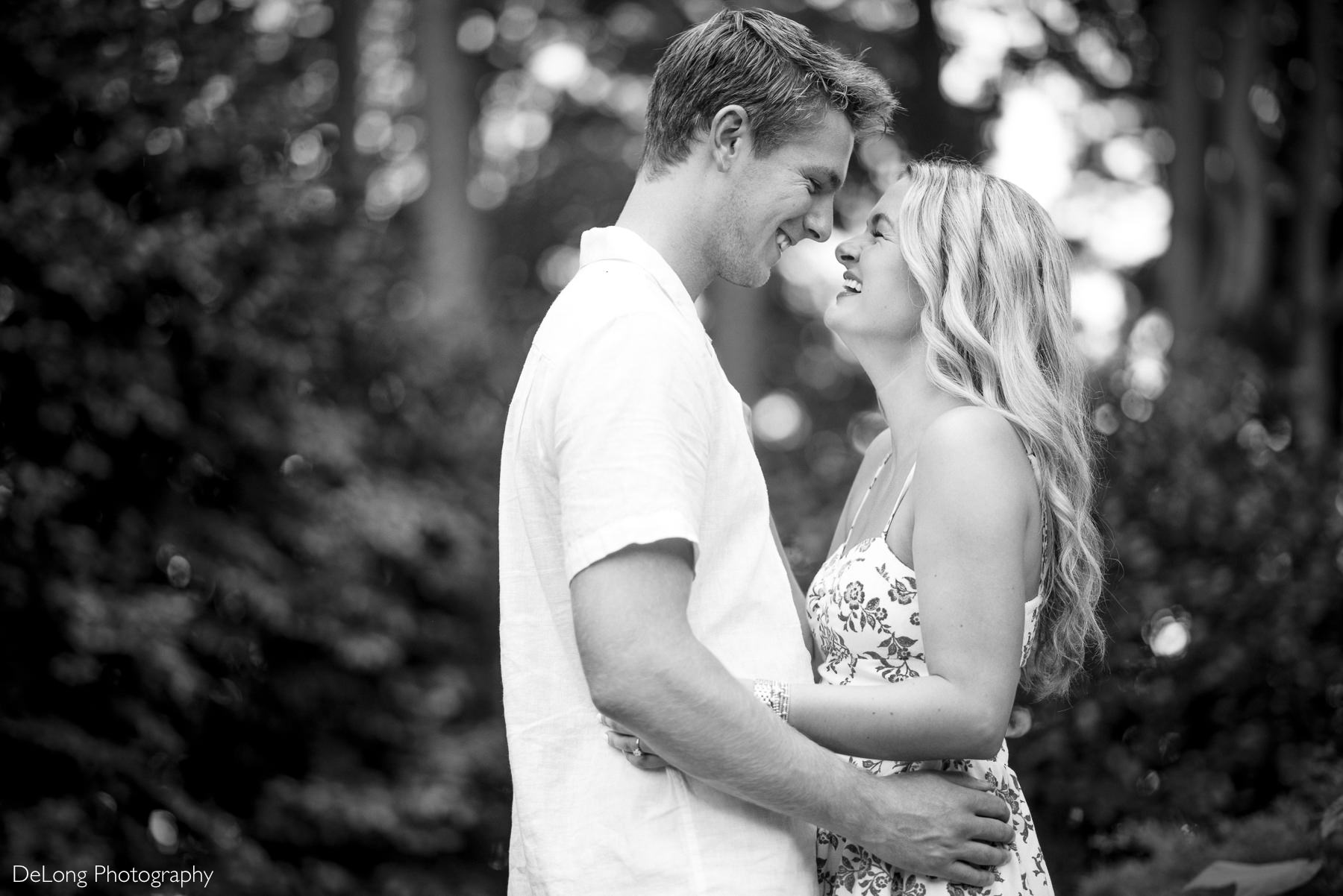 Black and white portrait of an engaged couple during a WRAL Azalea Garden engagement session in Raleigh, NC, showing he couple giggling with their faces close to each other. Captured by DeLong Photography a North Carolina engagement photographer.