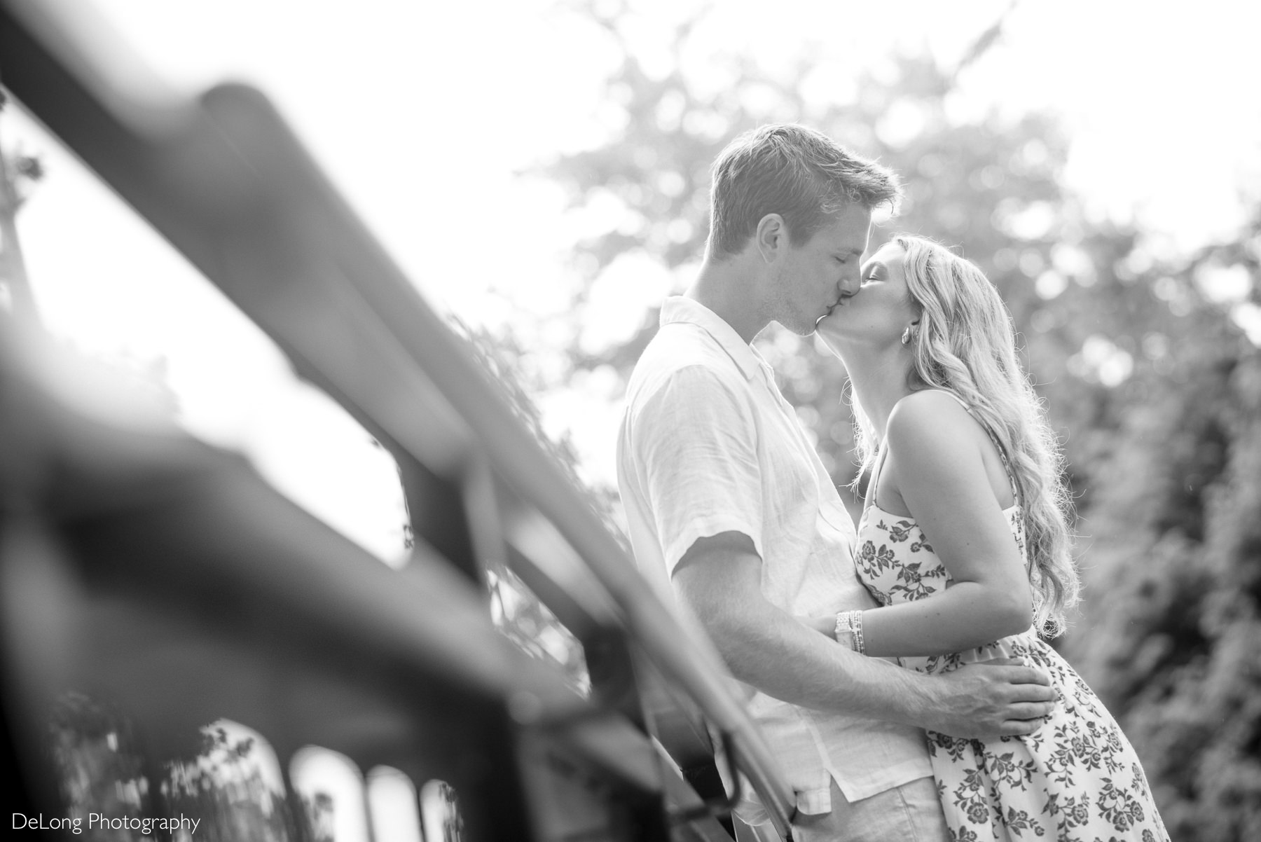 Engaged couple kissing on the bridge in the WRAL Azalea Garden surrounded by greenery in Raleigh, NC—captured by DeLong Photography, a top Raleigh wedding photographer highlighting the most romantic and natural photo locations in the Triangle.