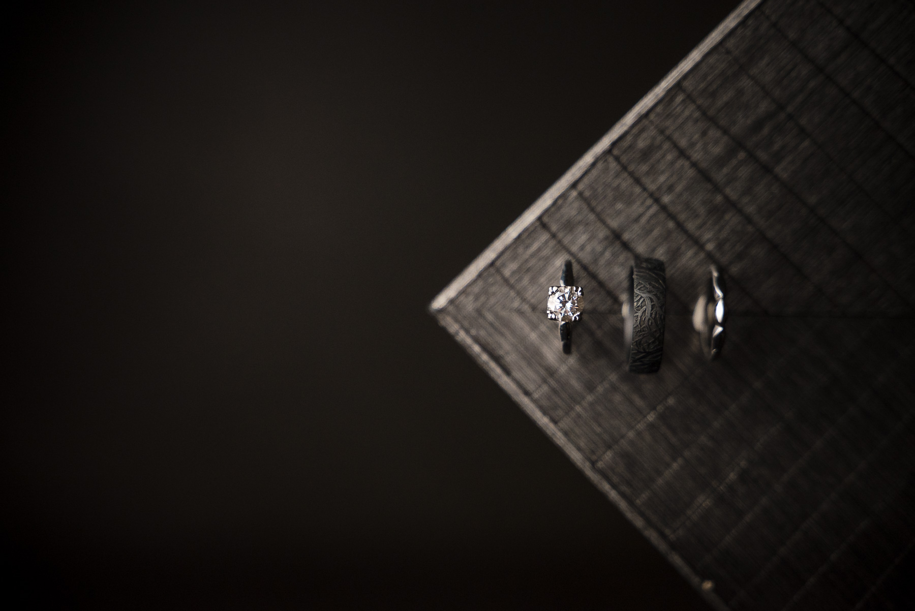 Wedding rings photographed during bridal details at Camelot Meadows in Charlotte, NC, featuring a diamond engagement ring, engraved black wedding band, and groom's ring. Elegant wedding ring flat lay captured by DeLong Photography, a Charlotte wedding photographer.