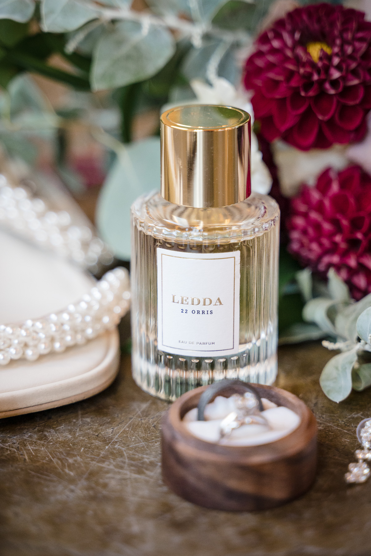 Bridal detail flat lay featuring wedding perfume, pearl bridal heels, wedding rings, and burgundy florals at a Camelot Meadows wedding in Charlotte, NC. Elegant wedding details photographed by DeLong Photography, a Charlotte wedding photographer.