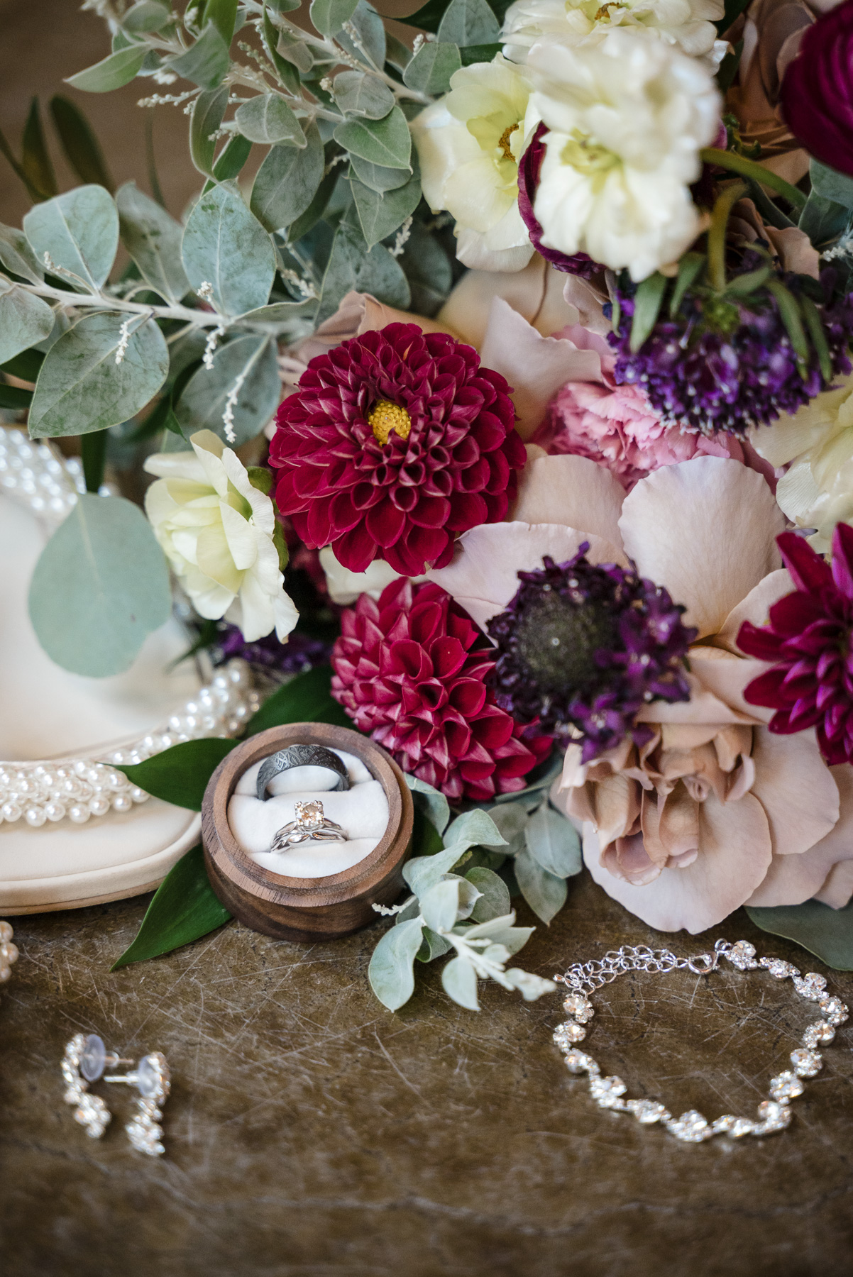 Wedding detail flat lay featuring the bride's bouquet with burgundy, blush, purple, and ivory flowers, wedding rings, pearl bridal heels, and jewelry at a Camelot Meadows wedding in Charlotte, NC. Romantic fall wedding details photographed by DeLong Photography, a Charlotte wedding photographer.