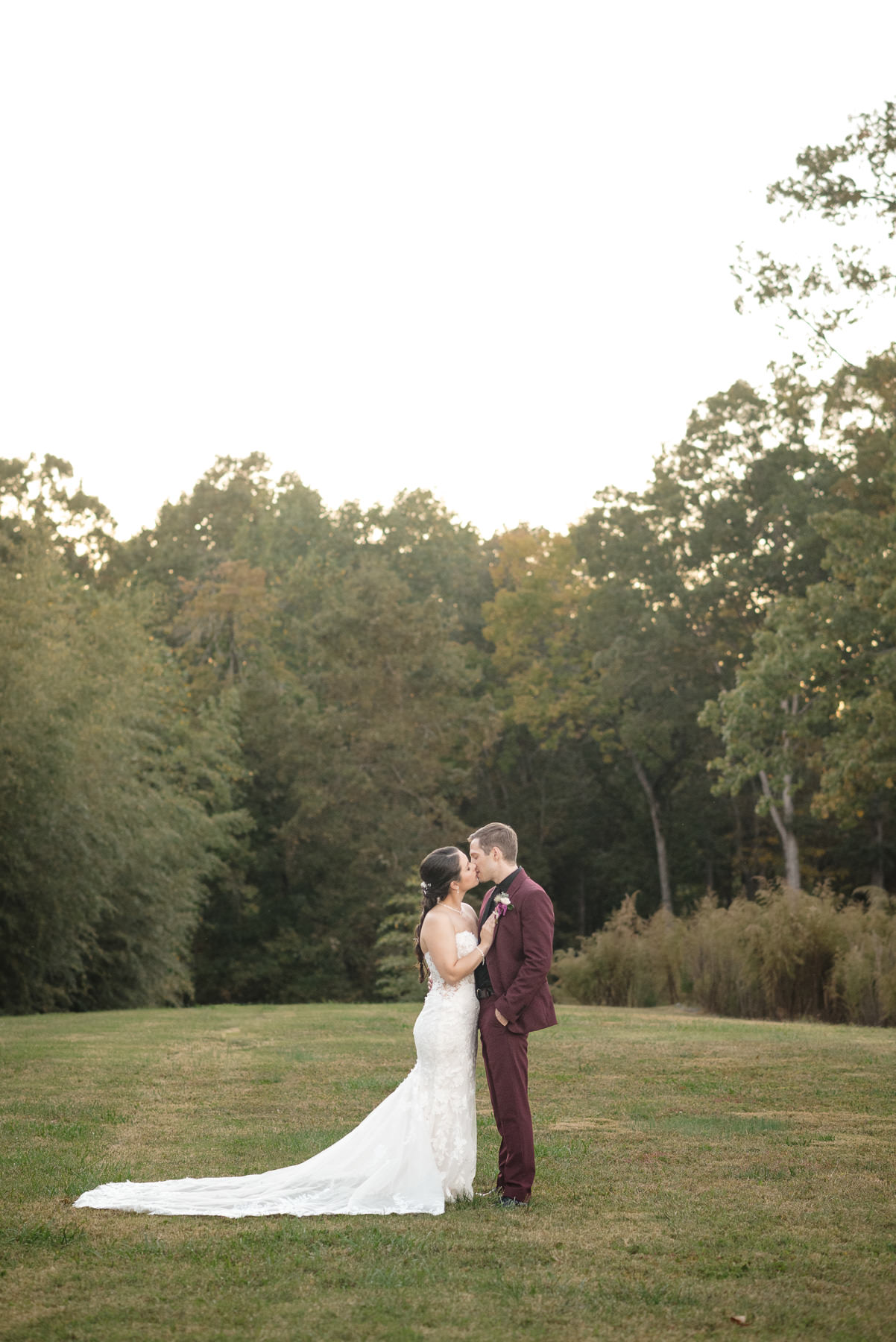 Bride and groom share a romantic kiss during golden hour portraits on the lawn at Camelot Meadows in Belmont, North Carolina. Captured by DeLong Photography, this elegant outdoor wedding portrait showcases the venue's scenic landscape and timeless wedding photography for Charlotte-area couples.