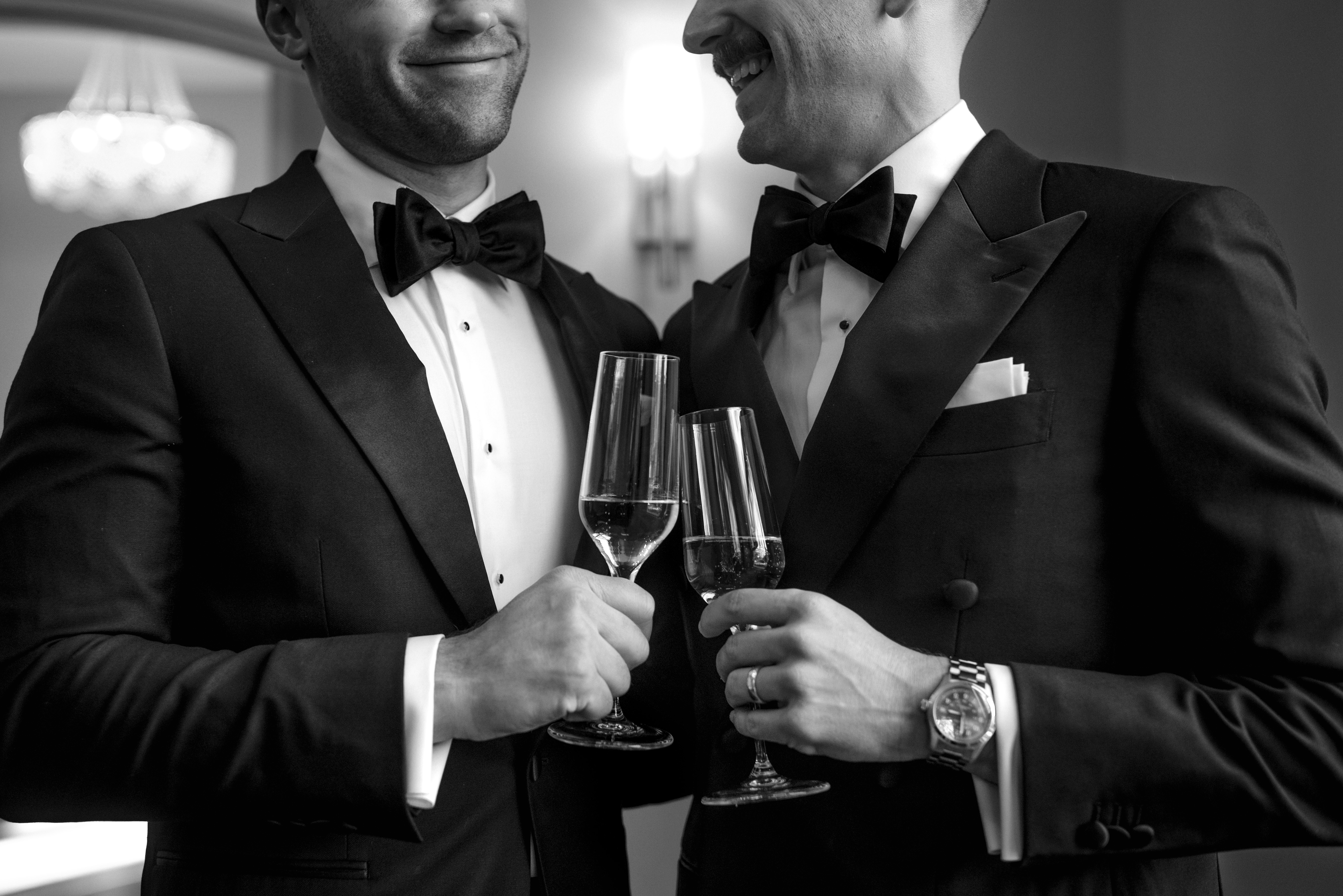 Two grooms in black-tie tuxedos toast with champagne at VanLandringham Estate during their elegant Charlotte, NC wedding reception.